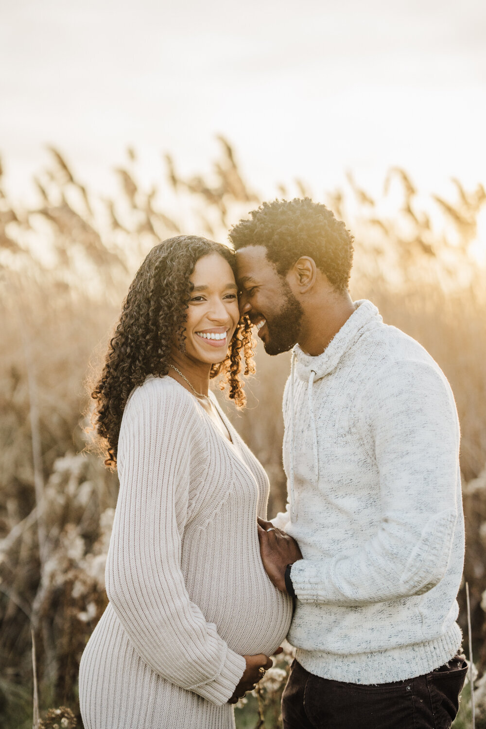 dad whispers in moms ear and they laugh together with golden grasses for boston maternity photoshoot
