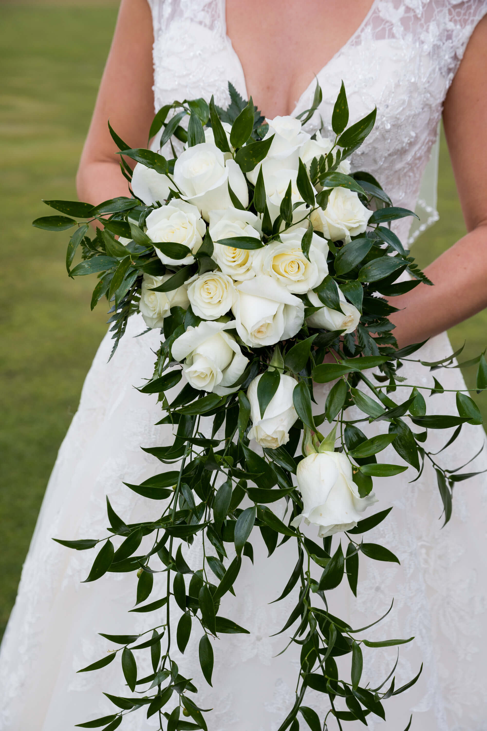 A cascading bridal bouquet of ivory roses and deep green foliage rests against the lace of a bride’s wedding dress. The bouquet’s elegant design complements the classic, timeless style of this Jackson Hole wedding.