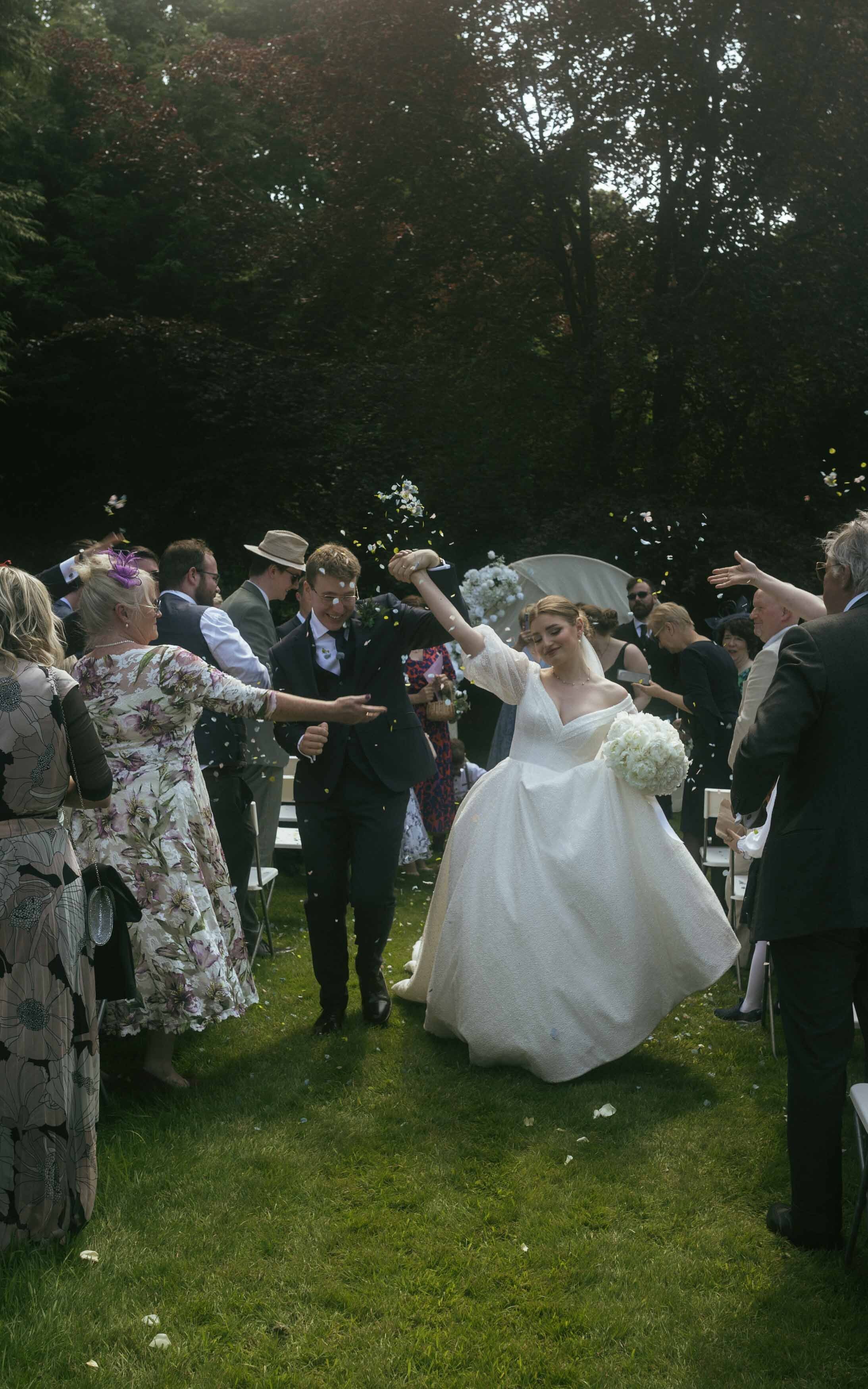 A lively and celebratory moment of a just married couple joyfully walking and dancing through a burst of confetti, marking the start of their new journey together