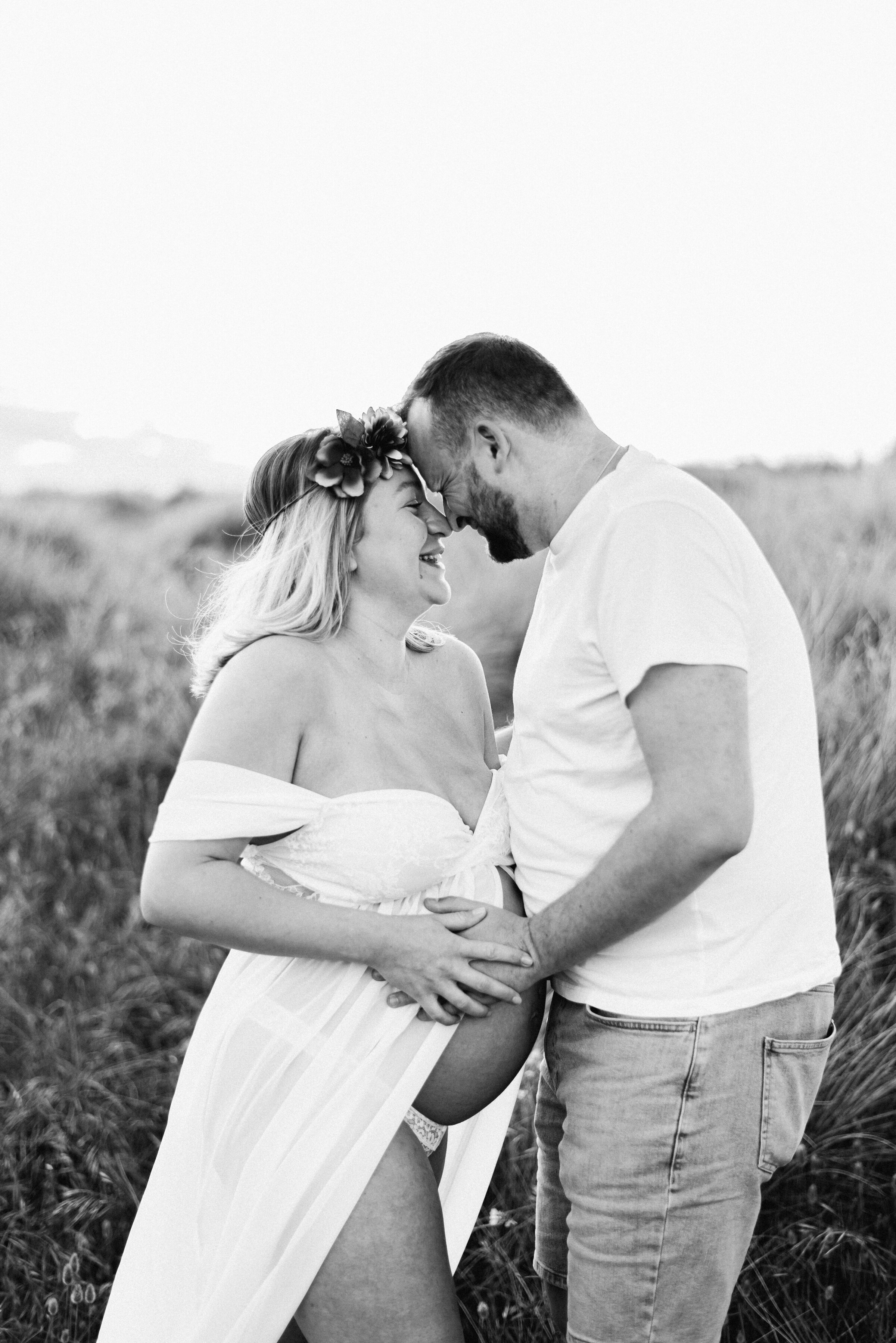 Women and Man holding onto the mothers pregnant belly with their noses touching at maternity photoshoot in  Billingshurst