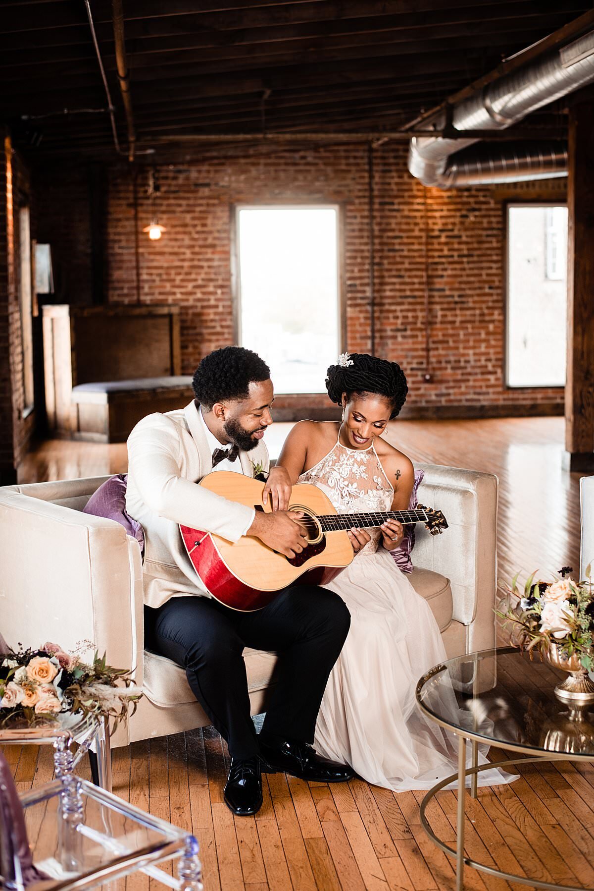 Couple sitting together on their wedding day in a cocktail setting playing the guitar