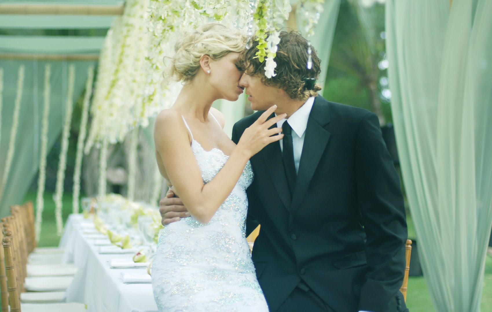 bride and groom kissing next to their table where guests will be seated with beautiful flowers and pearls.