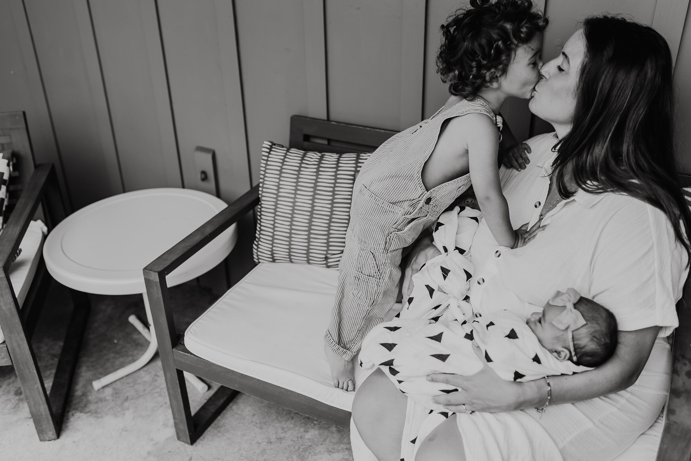 Black and White Photo of Mom Kissing Toddler While Holding Baby
