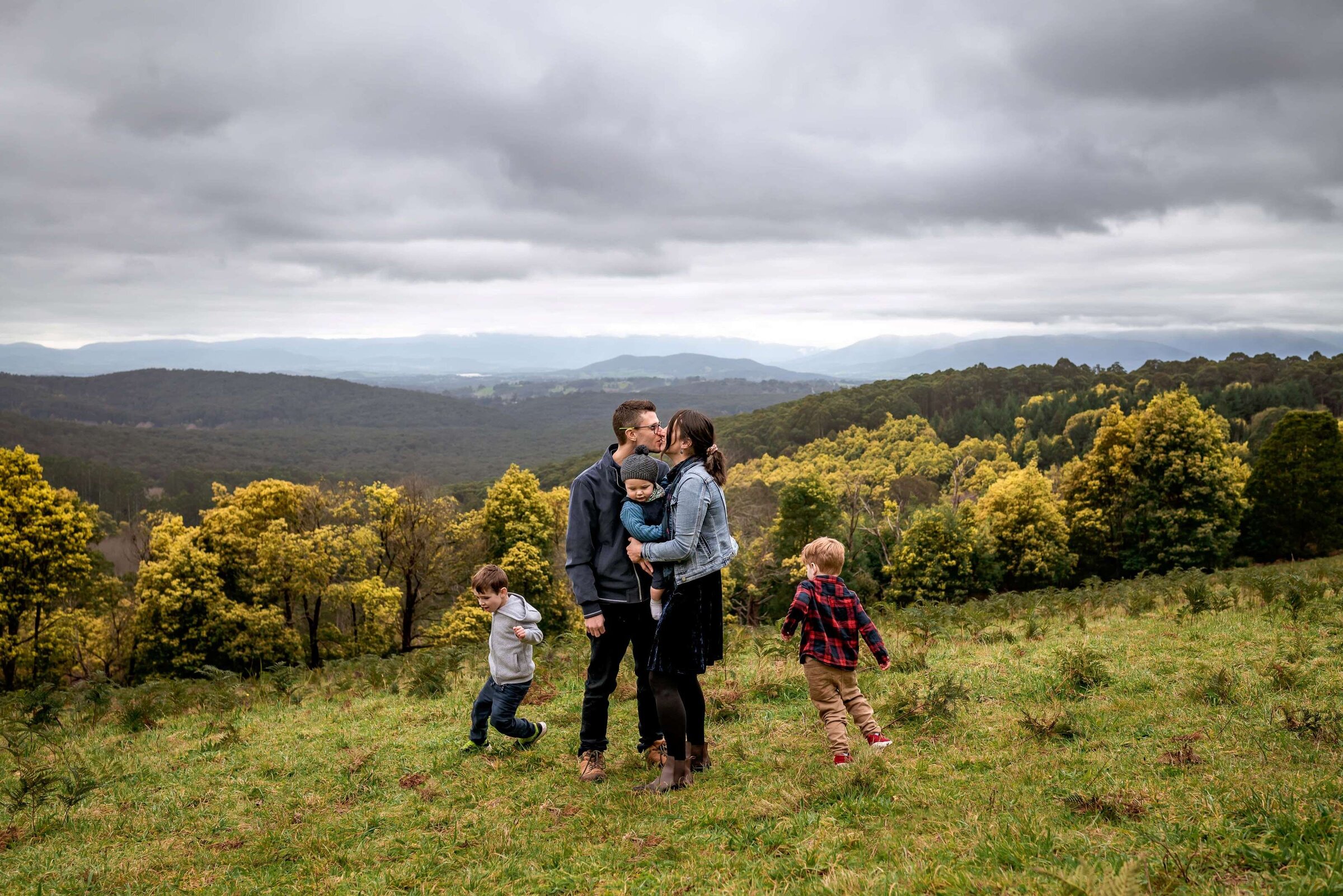 Parents with two toddlers running around them on a hilltop in Olinda