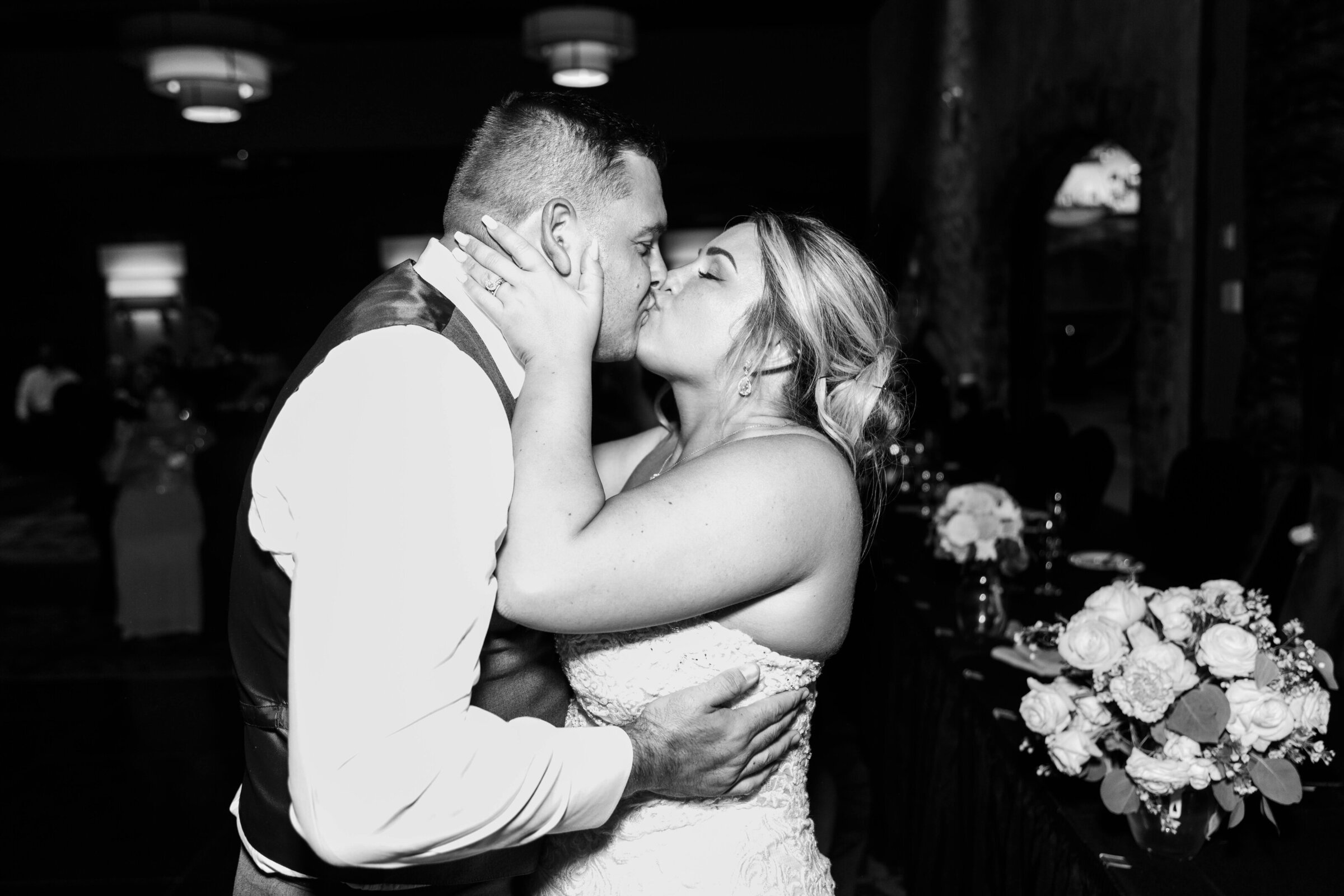 A black and white photo of a bride and groom kissing at their wedding reception.