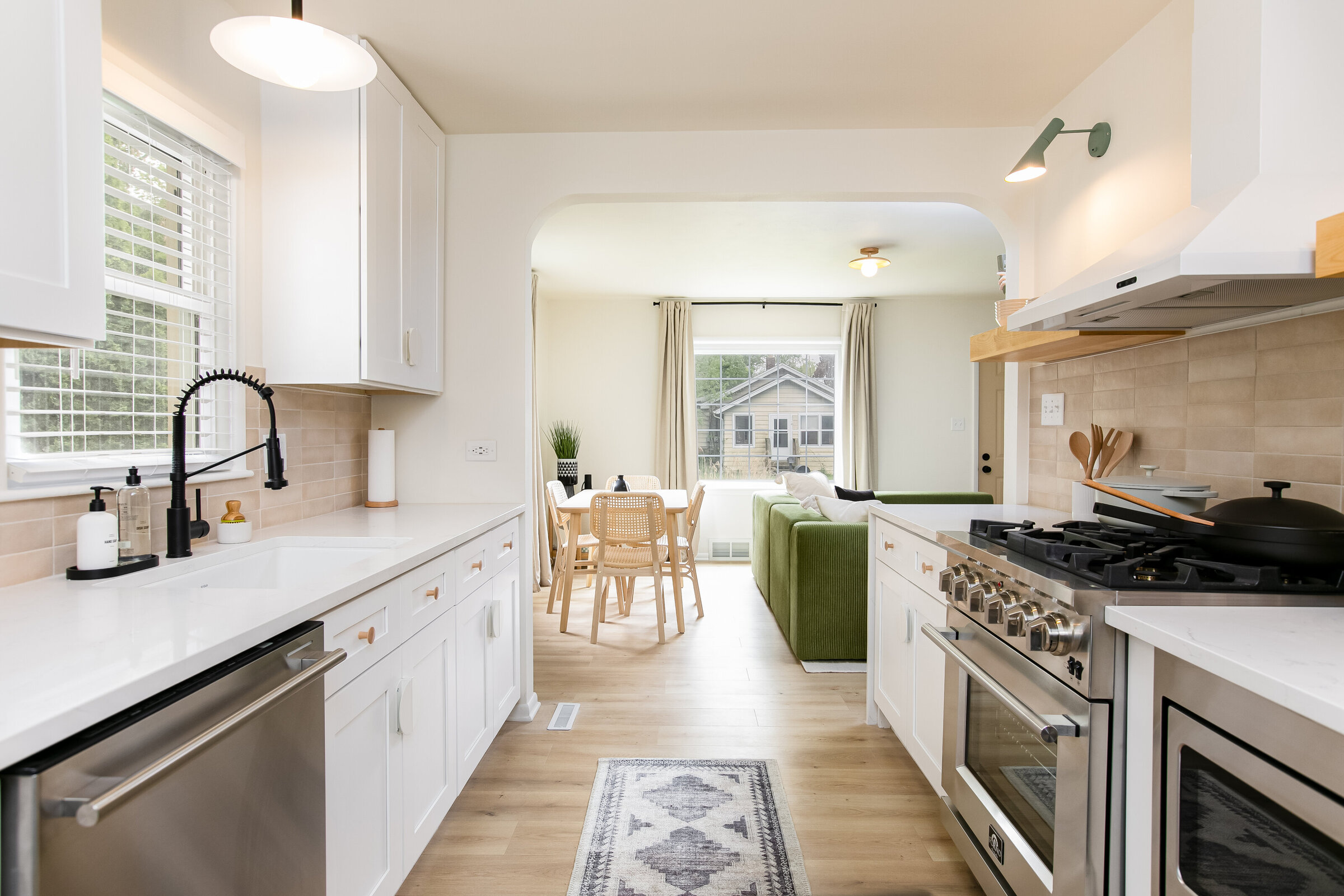 A clean, white kitchen with a view into a bright, airy dining room. The space features minimal decor, creating a serene and modern environment perfect for both cooking and dining.