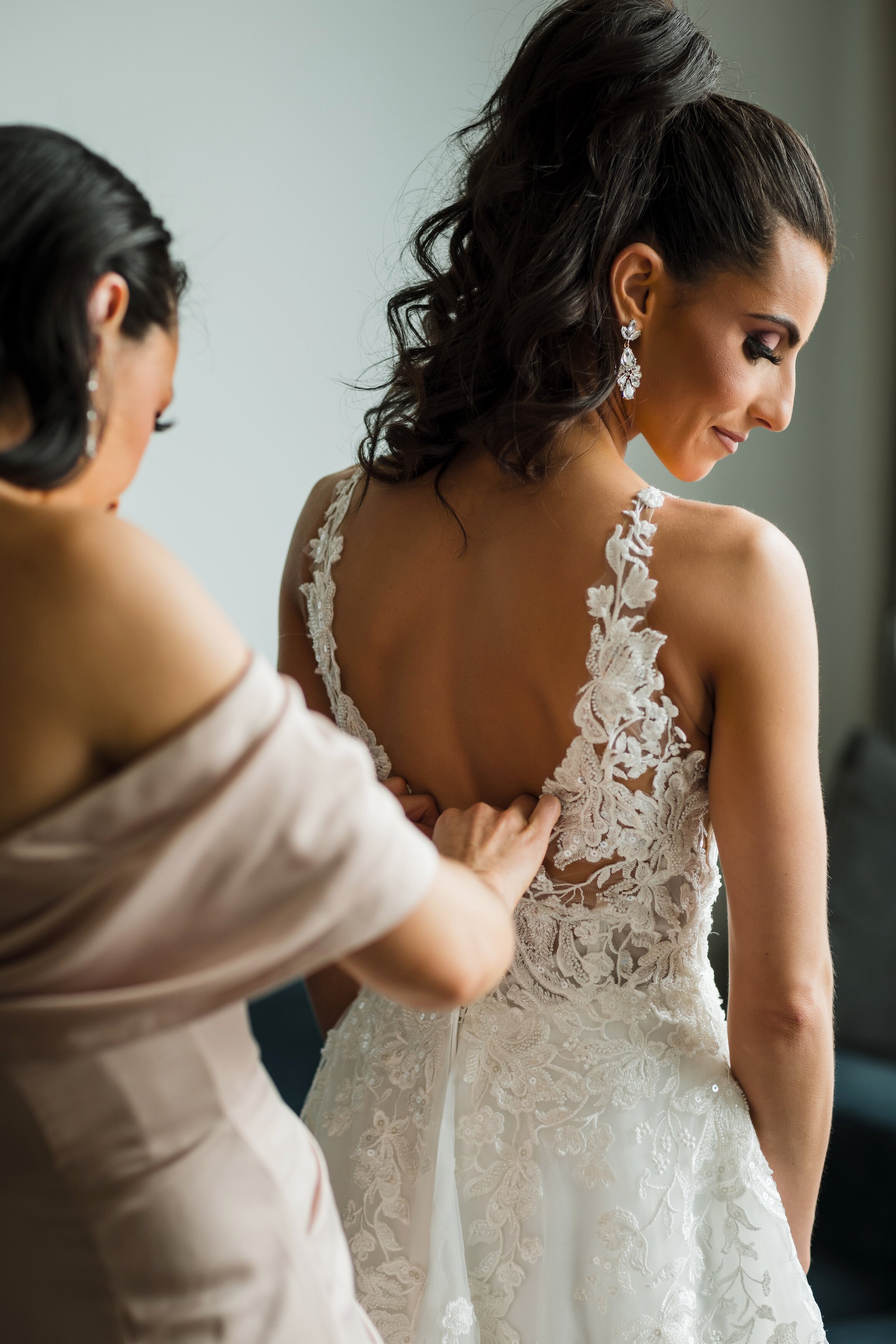 Gorgeous bride with a high curly ponytail looks calmly over her shoulder while getting dressed at Logan Hotel, Philadelphia