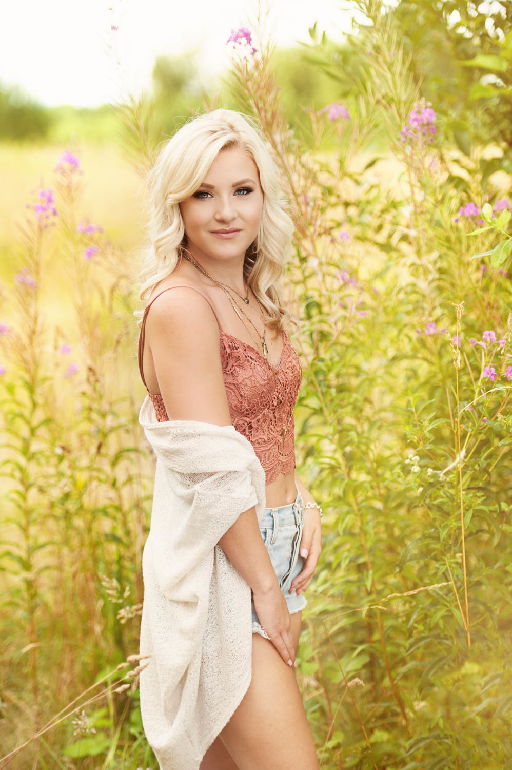 high school senior photo of girl in long green grasses with flowers