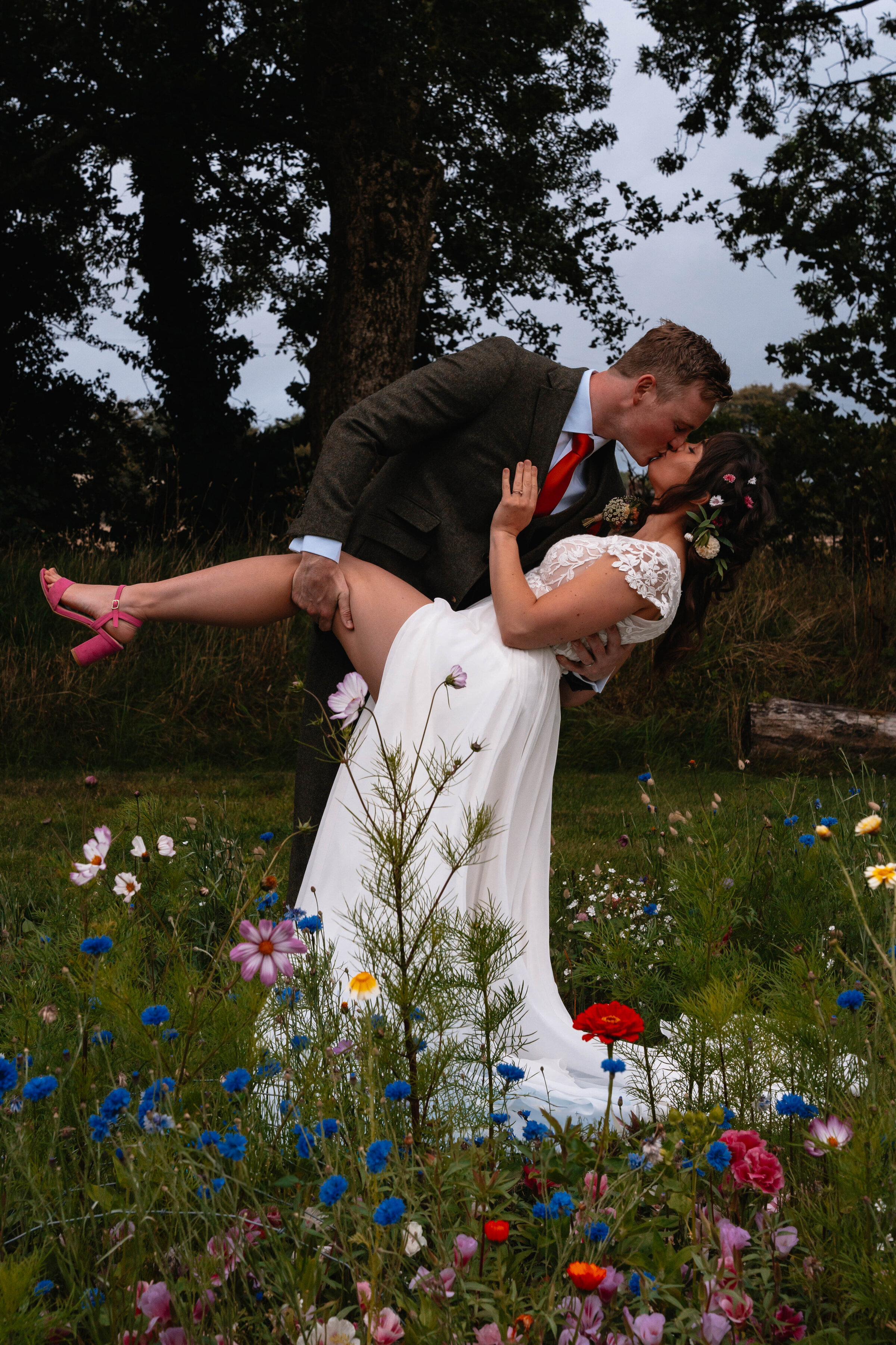 Bride and Groom in wedding attire in a dip kiss surrounded by wildflowers