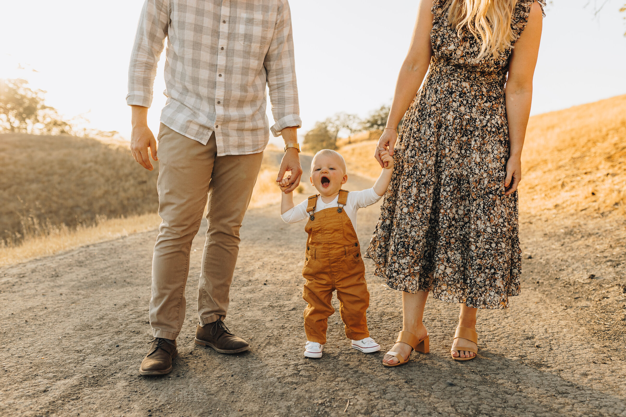 Parents hold the hands of their little boy as he walks