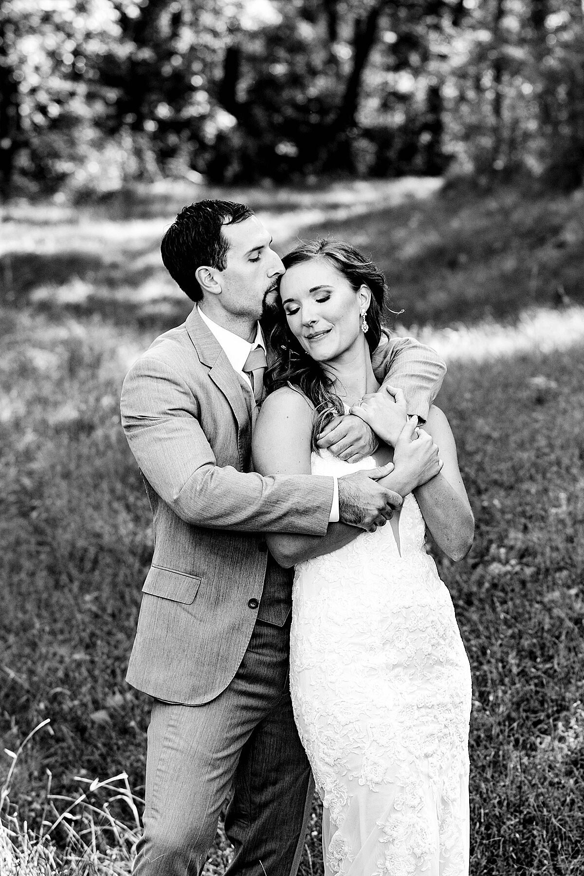 Black and white photo of groom embracing bride and kissing her on the forehead