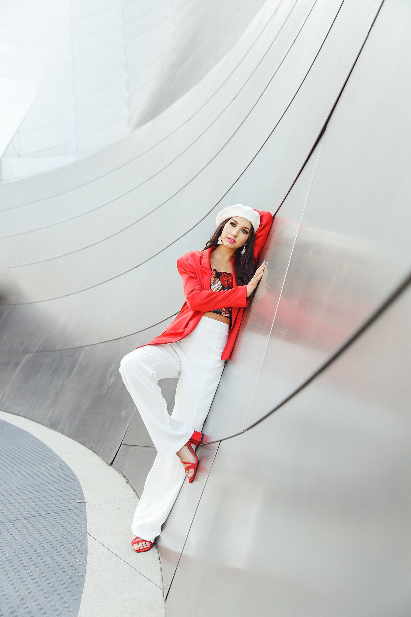 Striking girl in a red blazer and white beret leaning against the Walt Disney Concert Hall in Los Angeles California for a senior photoshoot. 