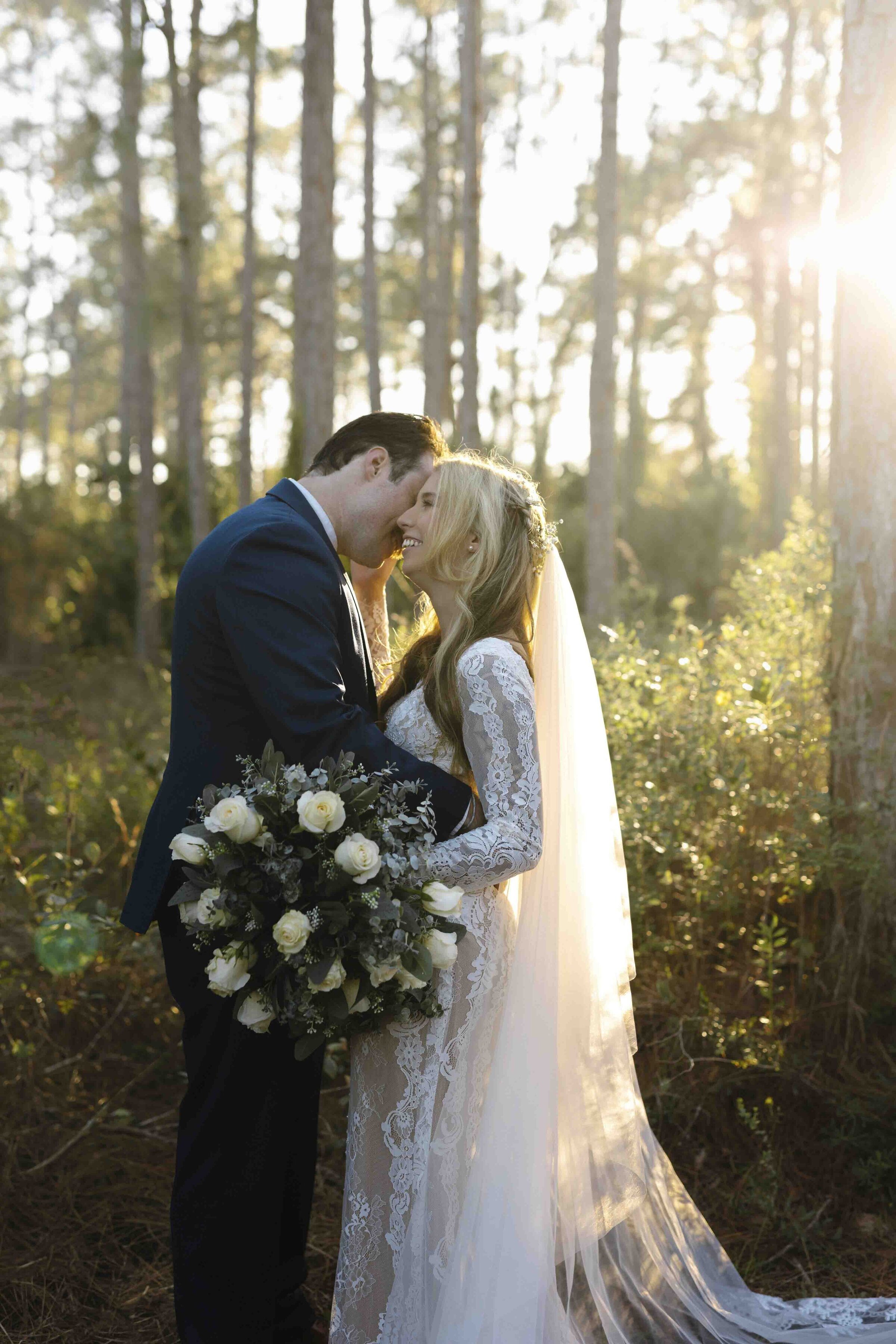 Groom kissing smiling bride holding flower bouquet