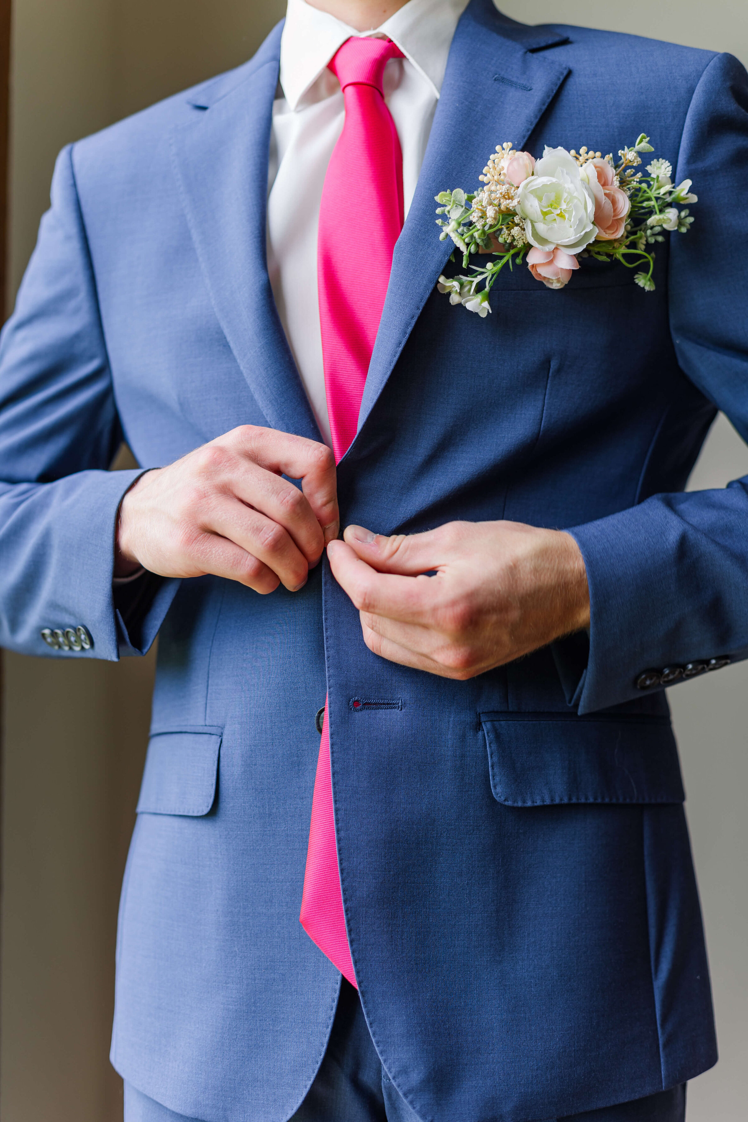A groom in a blue suit buttons his jacket - this is a cropped image of just his suit jacket.