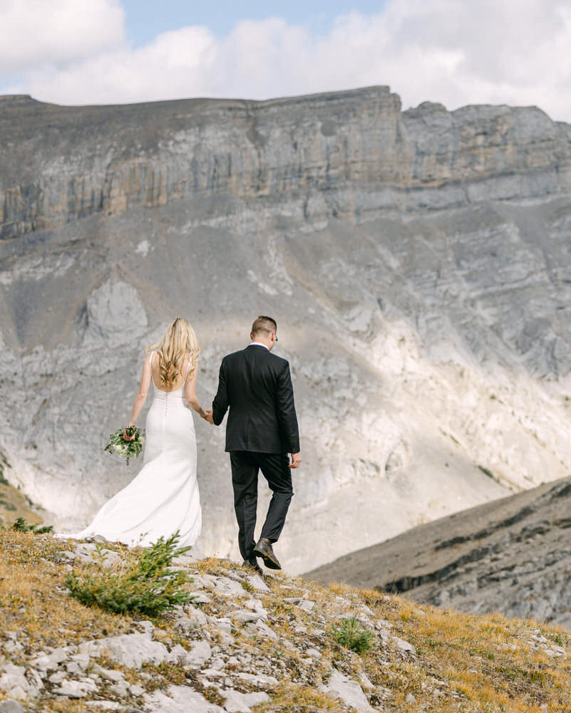 A breathtaking adventure elopement moment as the couple descends hand-in-hand down a rugged mountainside after arriving by private helicopter. Captured in the heart of the Canadian Rockies, this luminous photograph embodies the essence of adventure, romance, and the raw beauty of an intimate wedding in the wilderness.