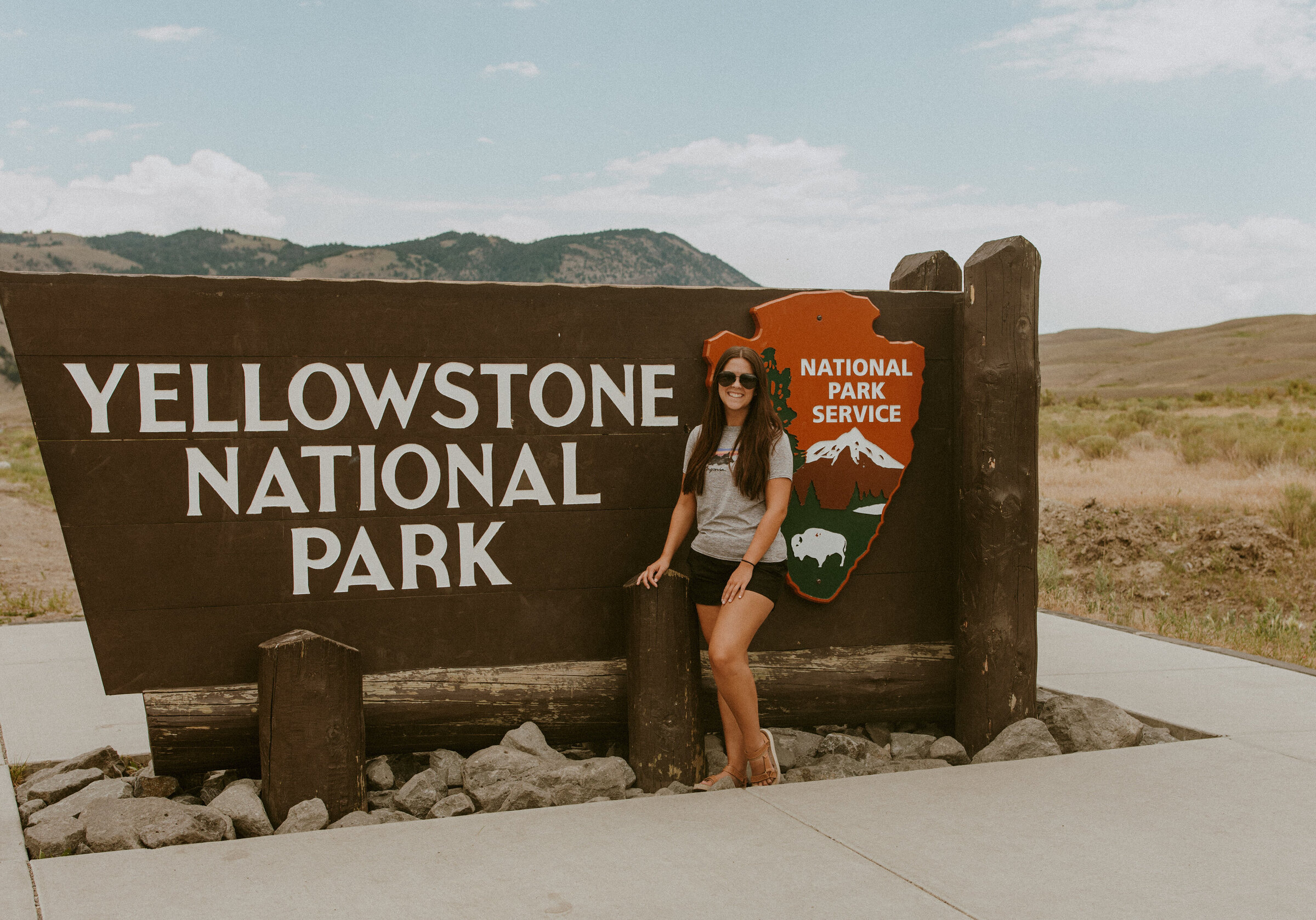 A girl standing by the welcome sign in Yellowstone National Park.