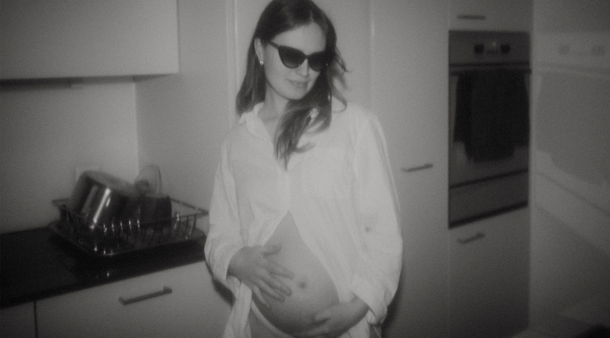 Lifestyle pregnancy photo of a pregnant woman. She is wearing black glasses and it is a trashy black and white photo.
