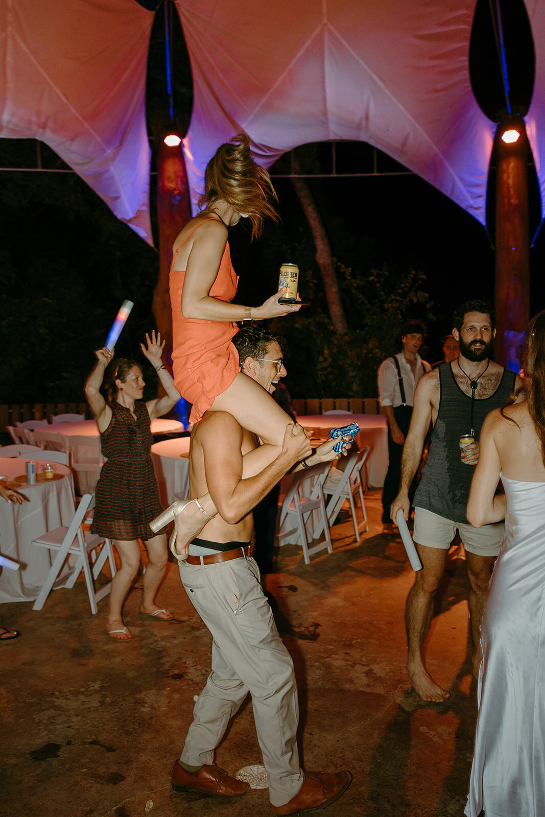A guest at a wedding puts a girl on his shoulders while they dance around.
