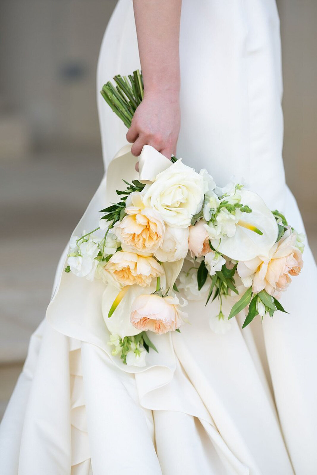 Bridal bouquet with garden roses and calla lilies, with part of a Morilee wedding dress visible in the background.