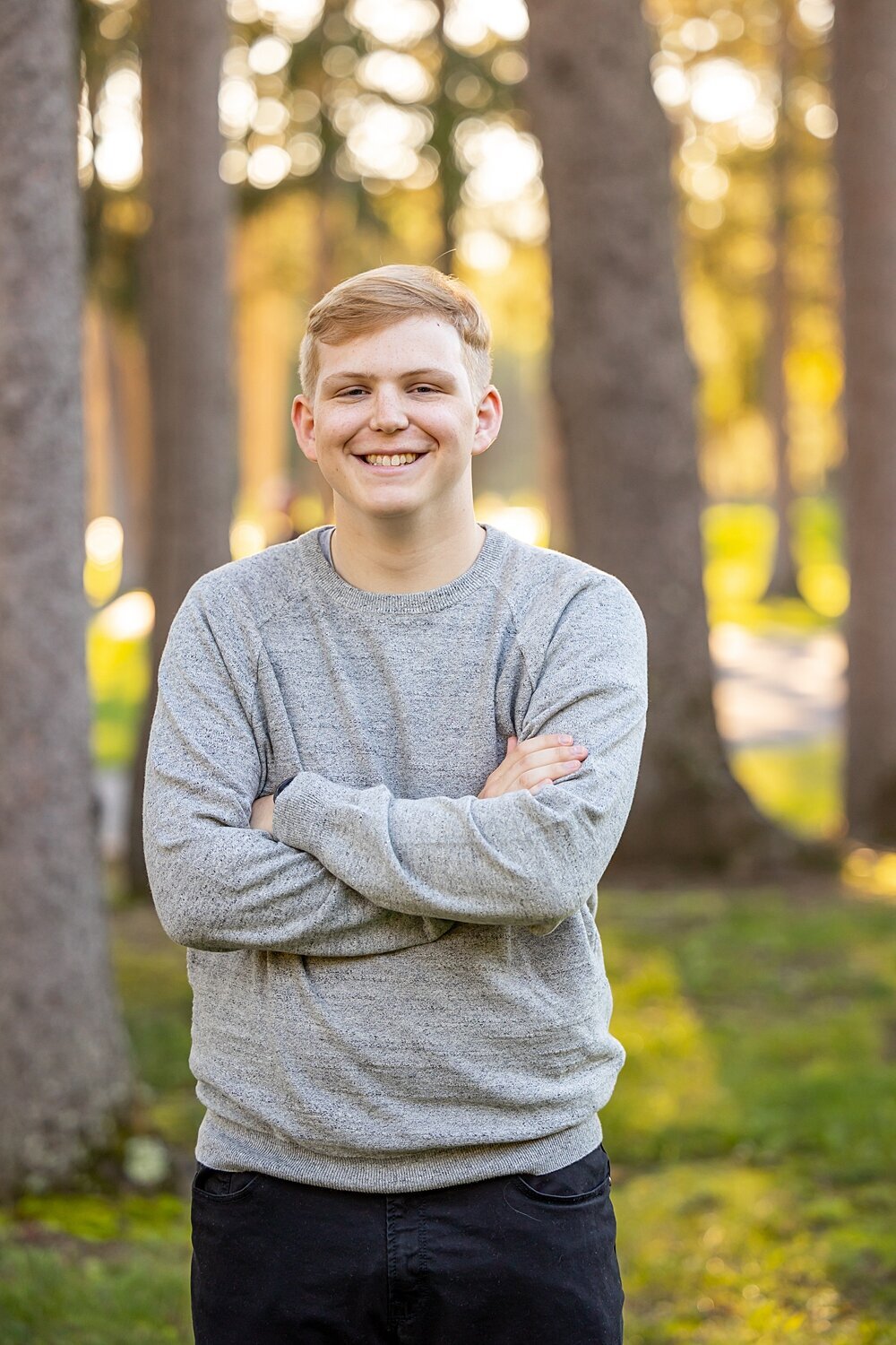 Fall senior boy crosses arms and smiles during fall senior session at Bensons Park in Hudson, New Hampshire