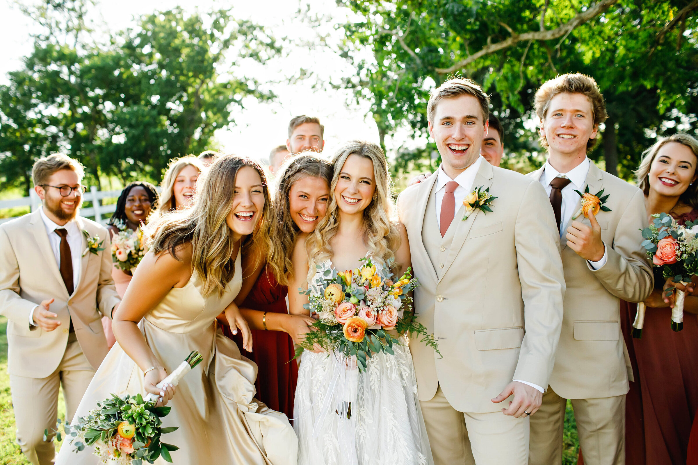 A bright and colorful wedding party photo. The bridal party is gathered around the bride and groom and everyone is smiling