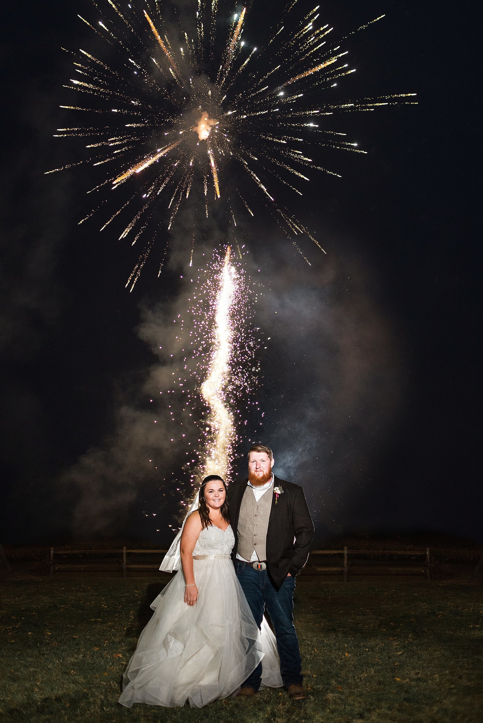 Bride and Groom standing in a field at night while they surprise their guests with a fireworks show