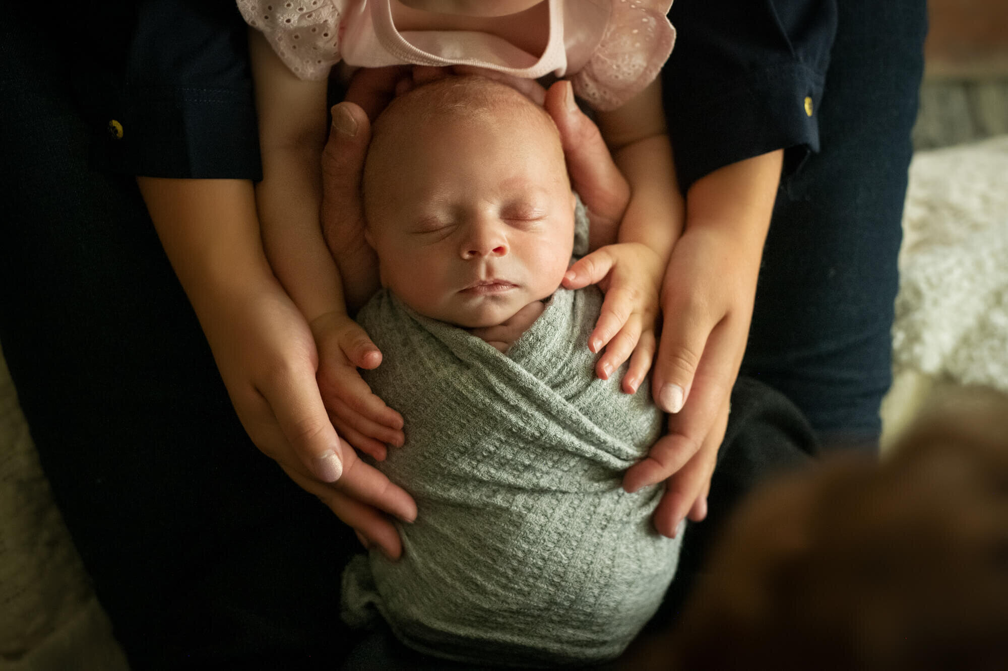 Baby boy in green wrap with parents hands placed on him