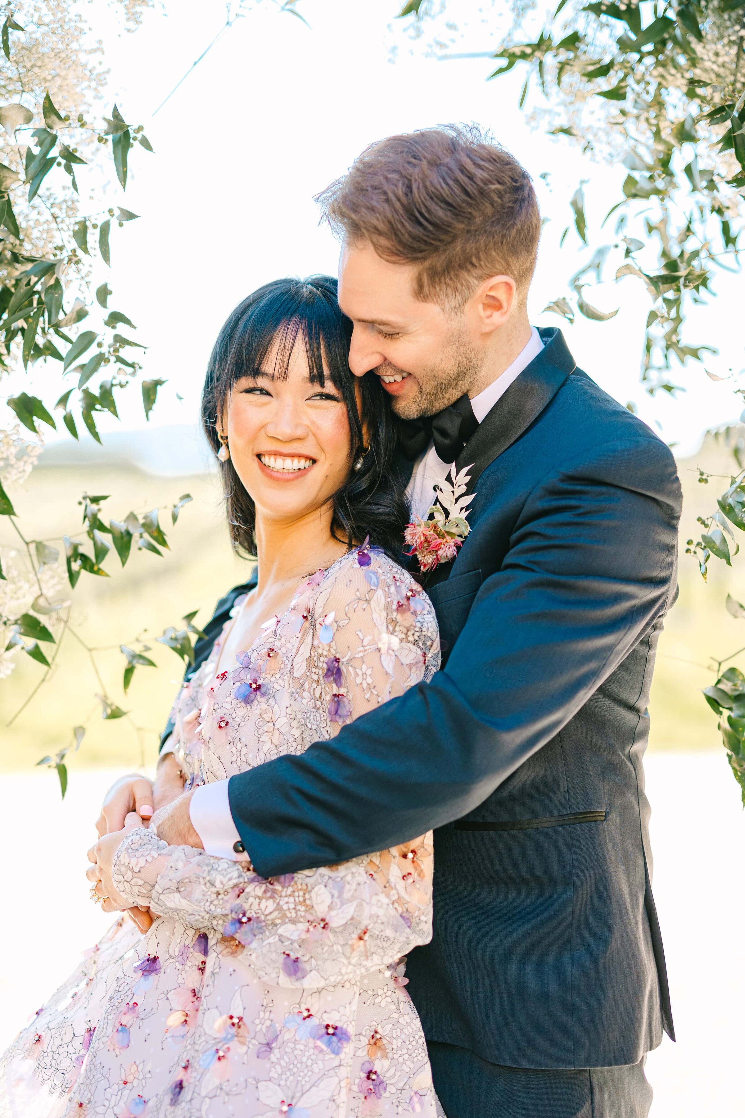 bride smiling while groom snuggles into her 
