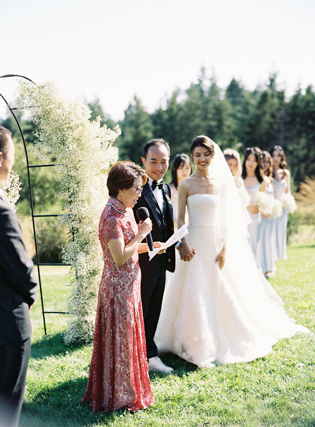 asian wedding mother of the groom gives speech during outdoor ceremony in red gown