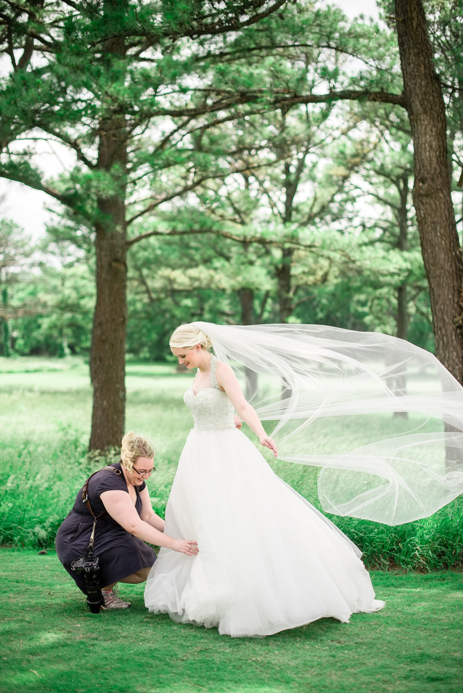 Behind the scenes photo of photographer adjusting the brides dress on a windy day at Stones River Country Club