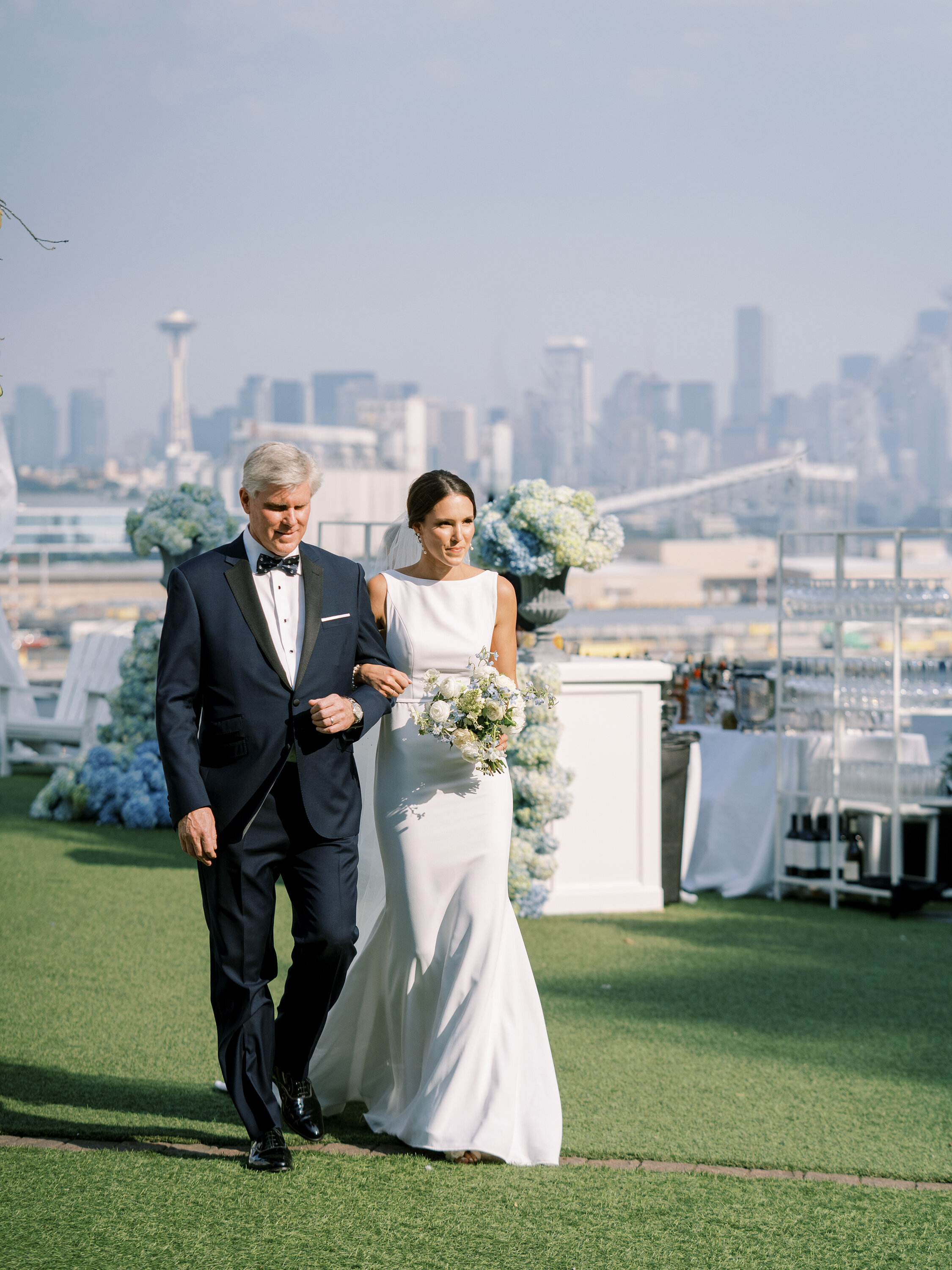 bride and her father arm in arm walking down the wedding aisle with downtown seattle in the background