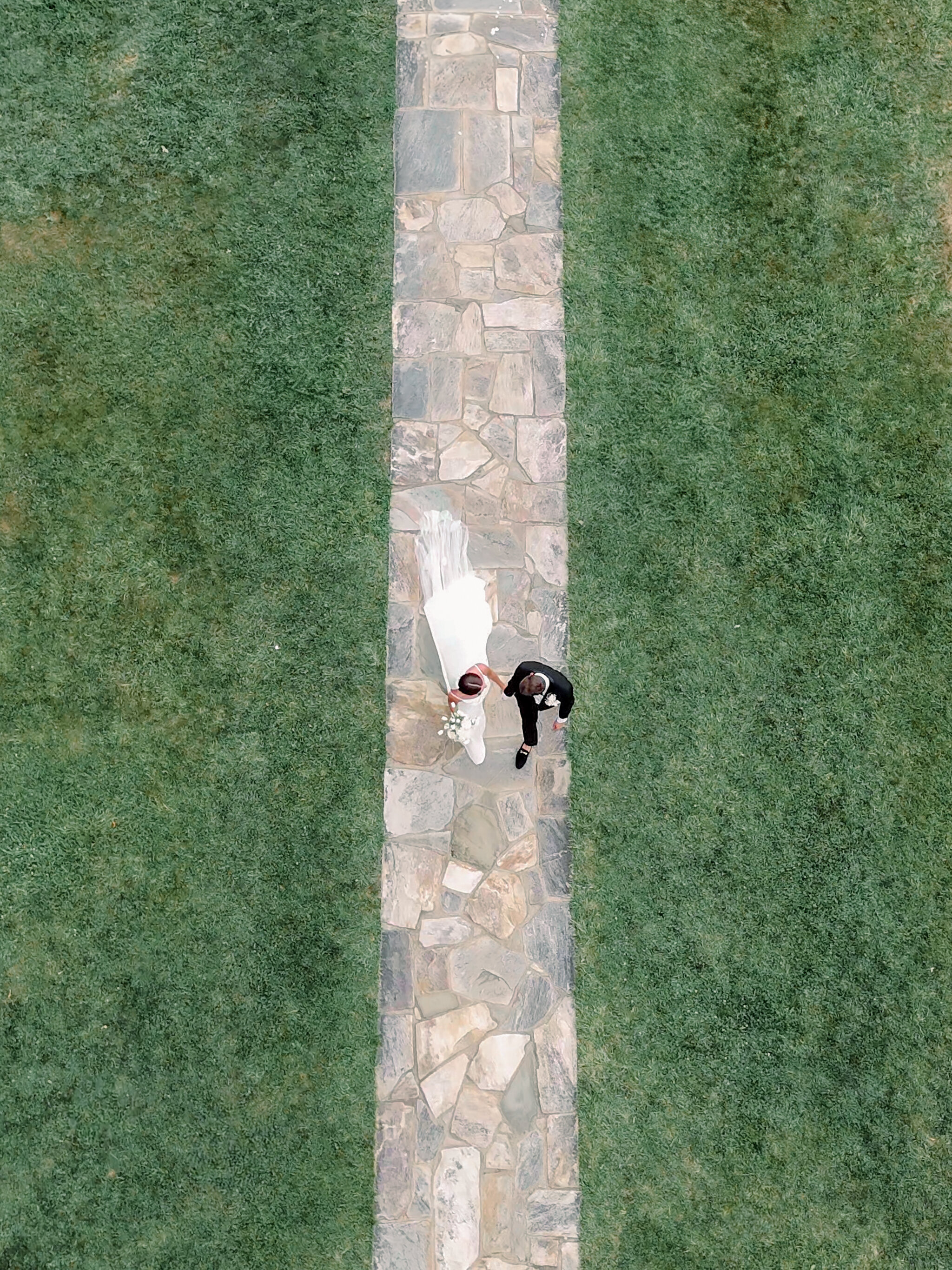 A drone photo of bride and groom walking hand in hand on a path at Rust Manor House.
