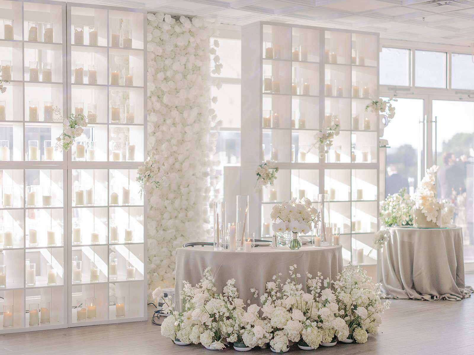Reception room with a wall of white florals, candlelit tables, and soft linens