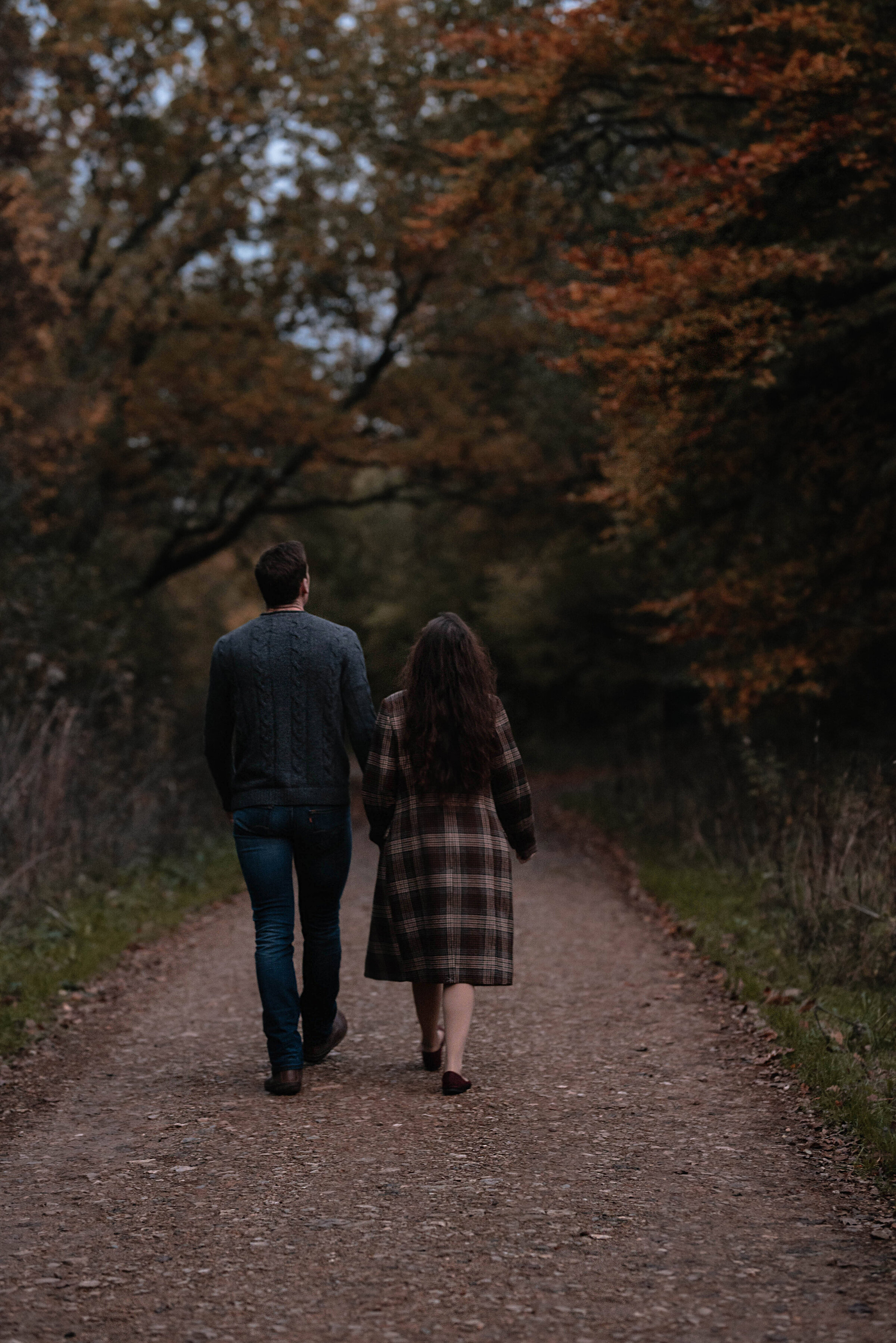 Man and woman walking away hand in hand surrounded by an autumnal scene of orange trees and fallen leaves