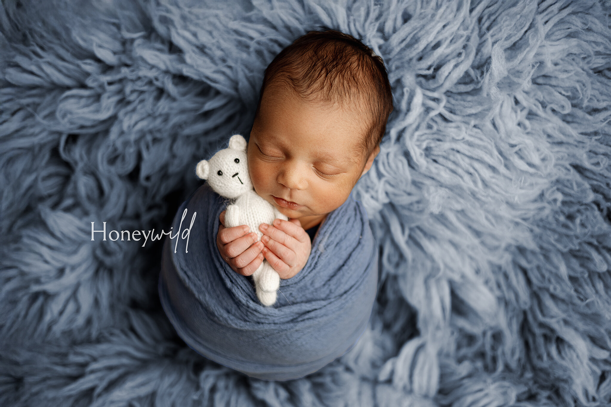 Grand Rapids newborn photography by Honeywild Photo: Newborn baby peacefully sleeping on a soft white blanket, wearing a rainbow knit hat. Capturing warm, timeless moments with professional newborn photography in Grand Rapids, MI.