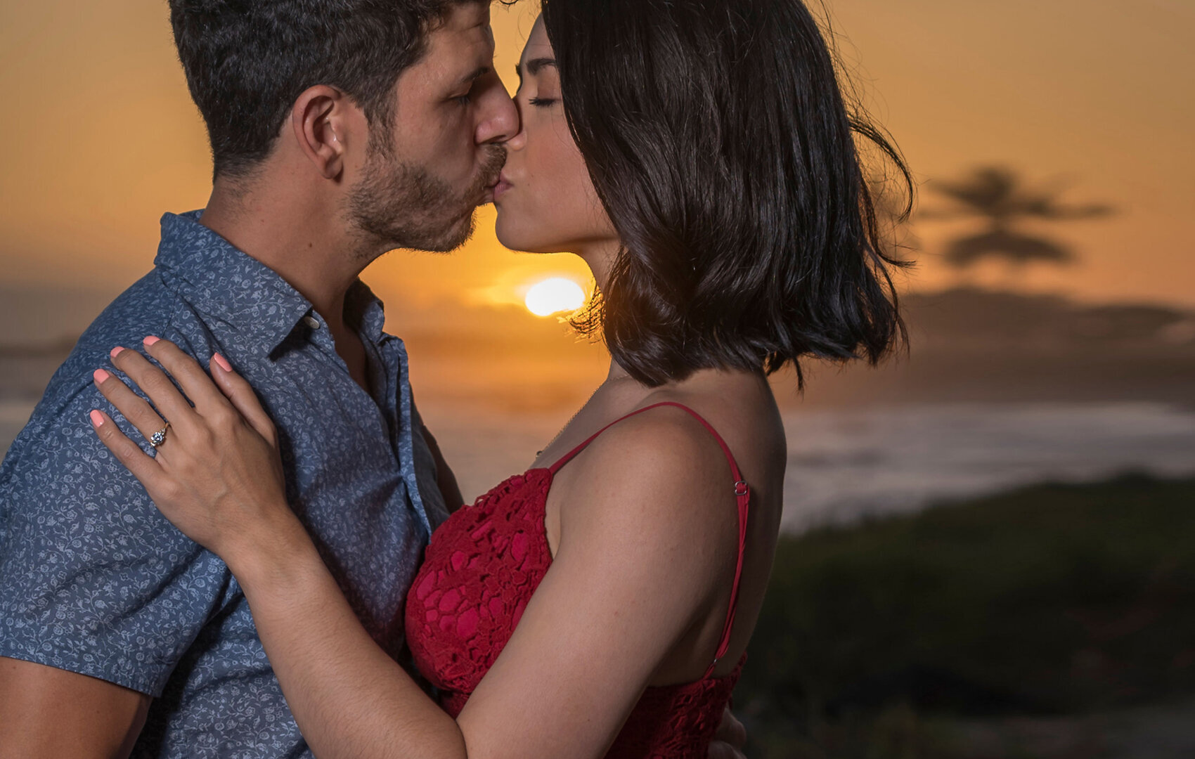 Kissing at sunset on Kauai  beach wearing a red dress.