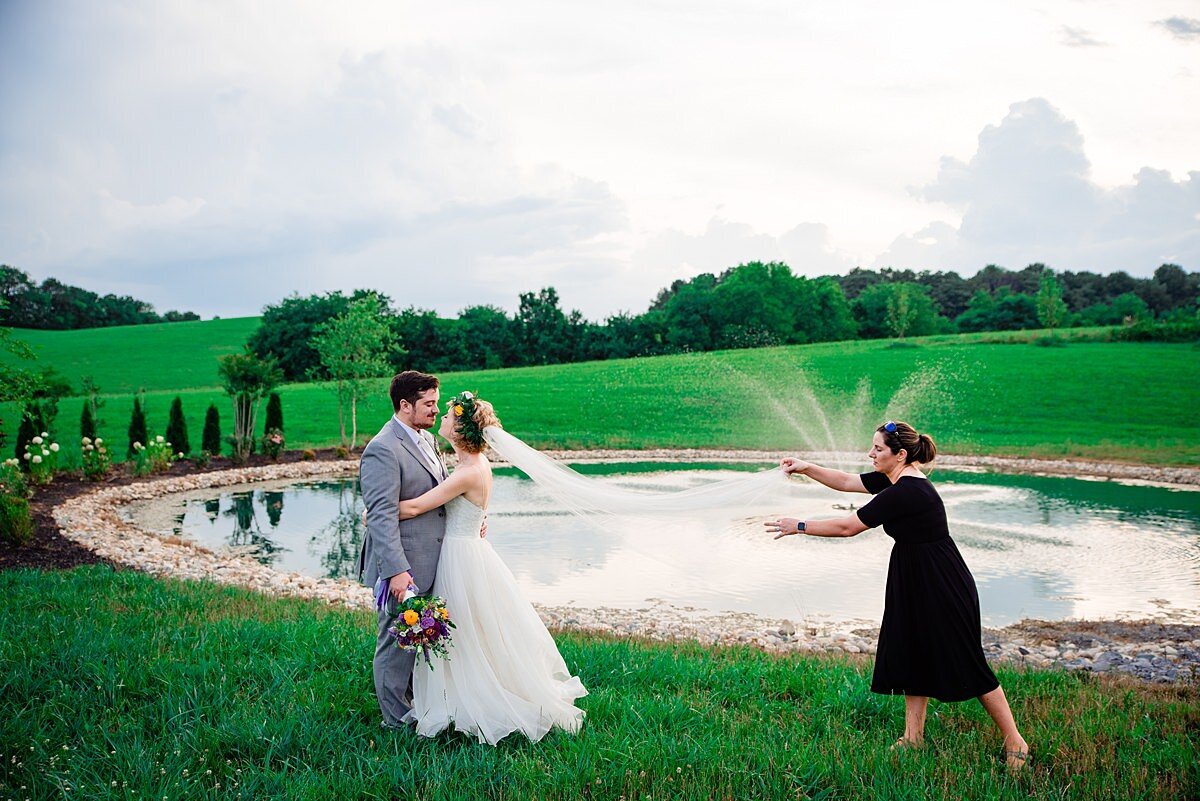 Photography assistant tossing brides veil for portrait in front of pond with a fountain