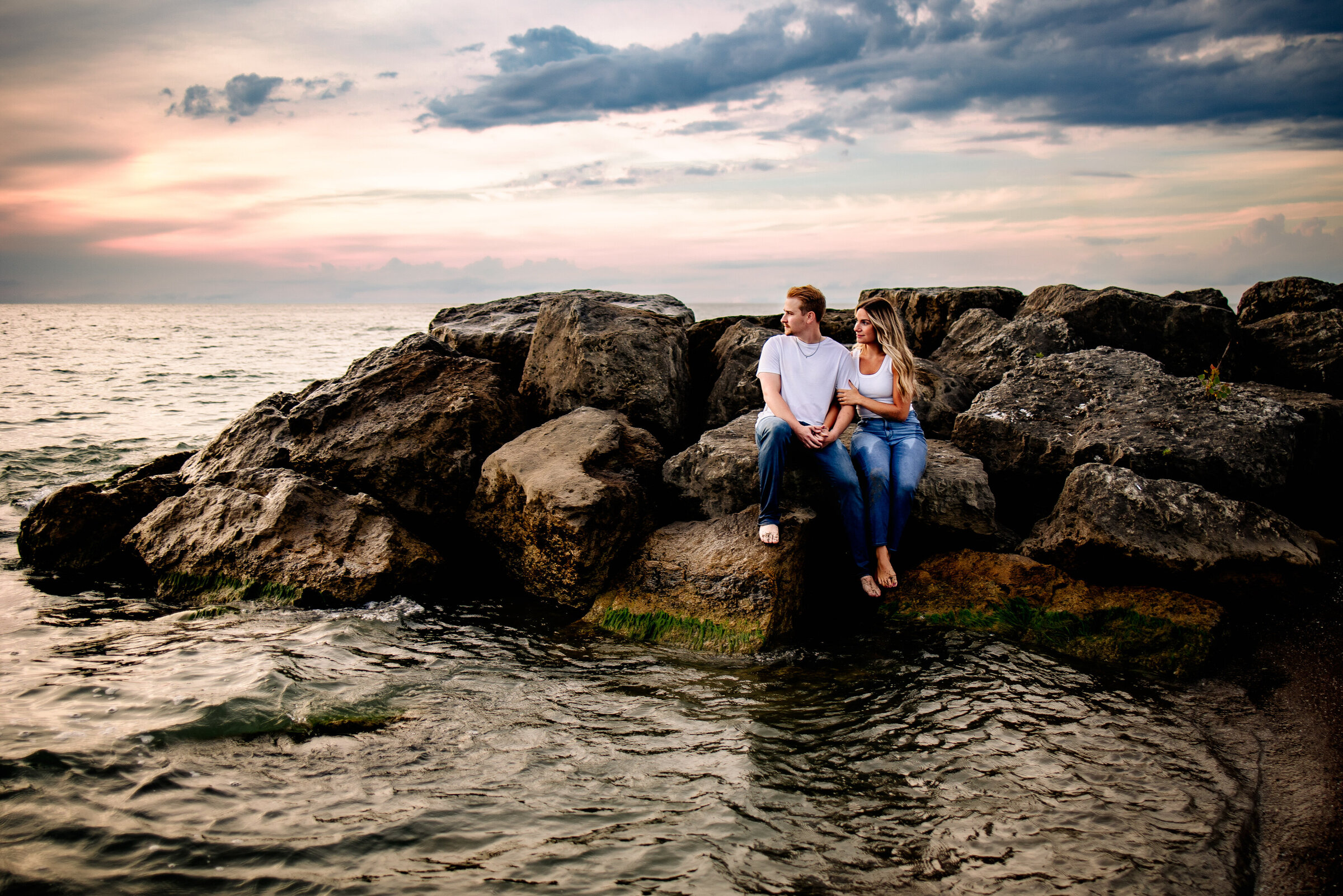 Couple sits together holding hands amongst a pile of large boulders Erie, PA