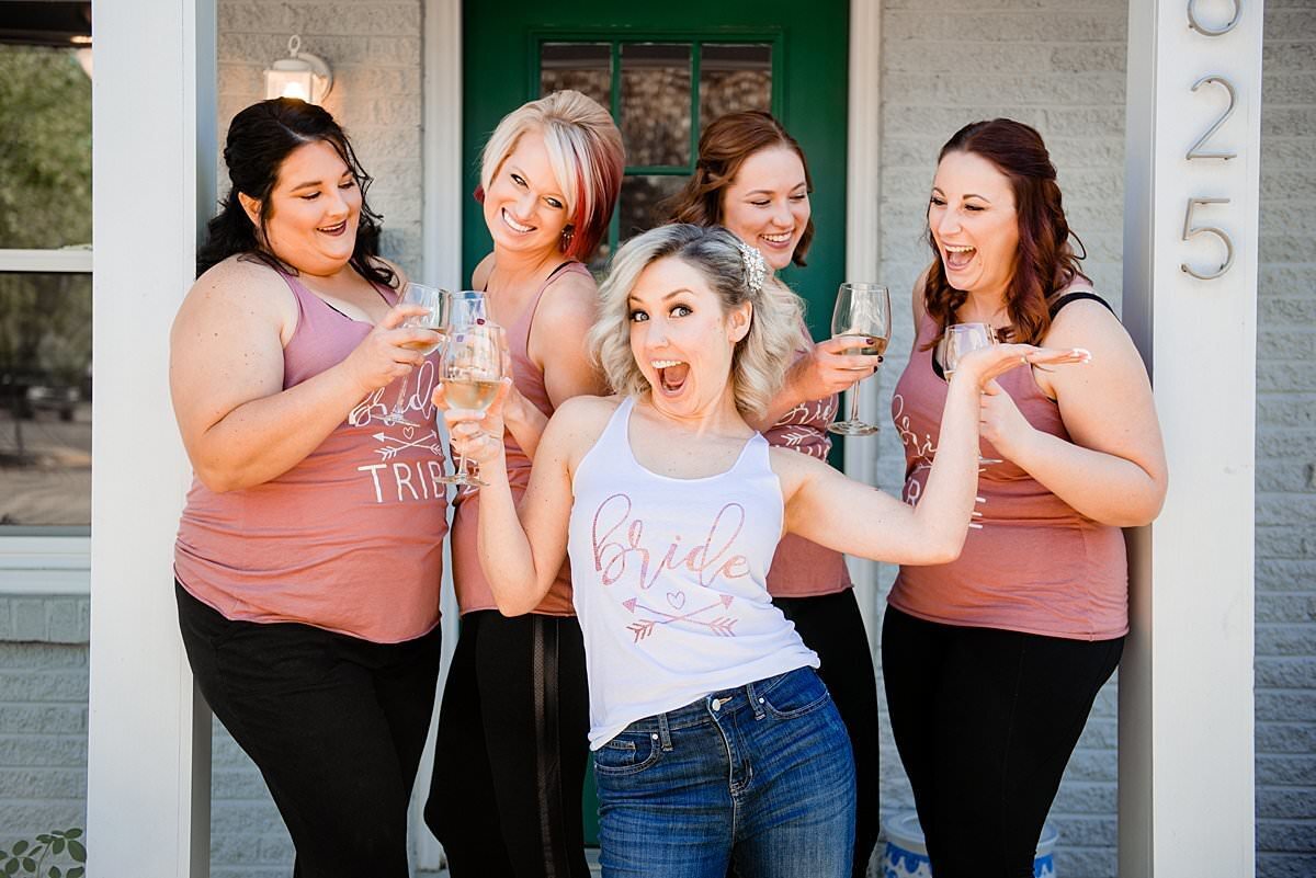 Bride on the front porch of her condo with her bridesmaids around her, they are all wearing bride tribe shirts and drinking wine
