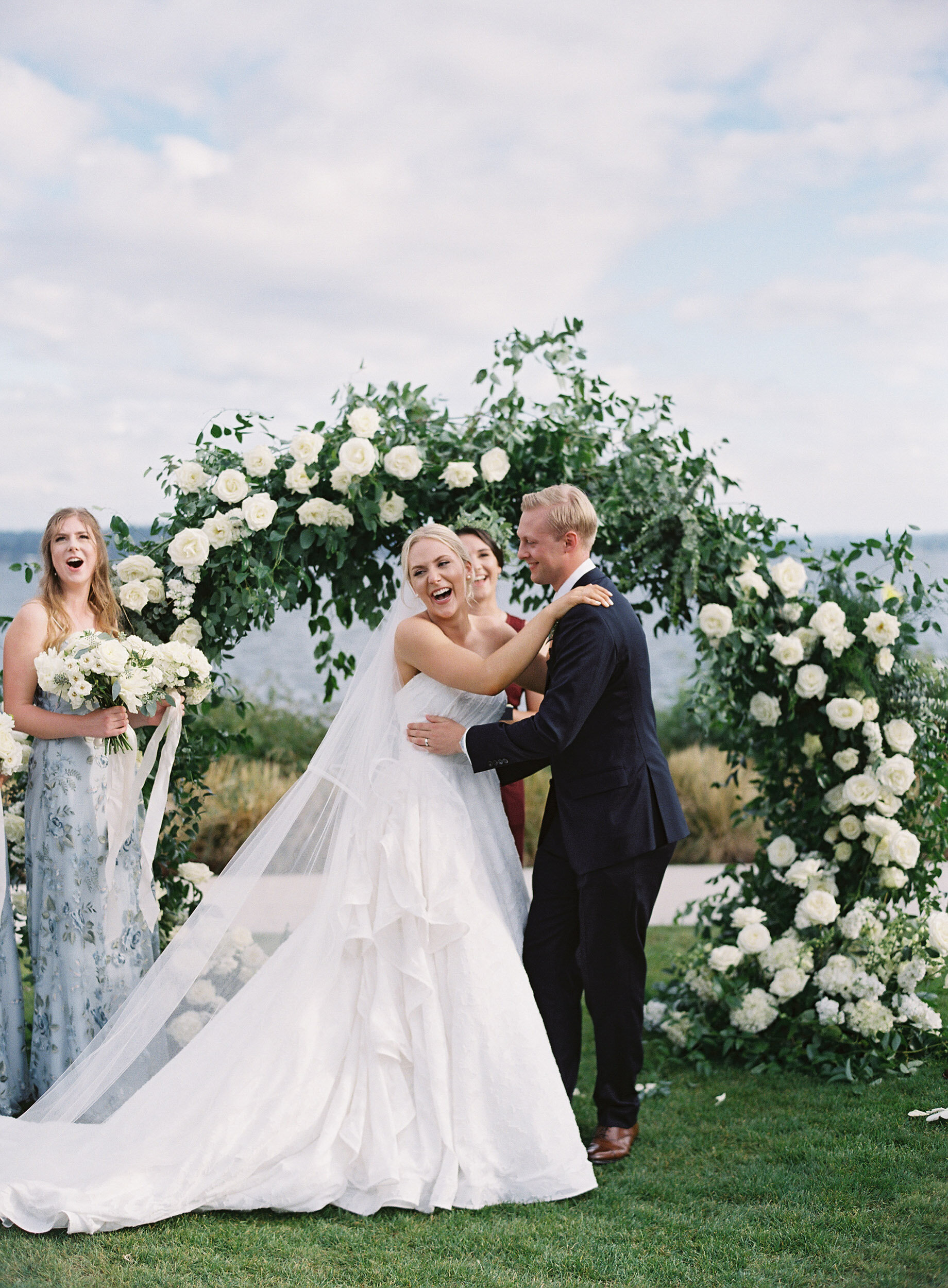 bride laughing with delight during her wedding ceremony with green and white floral arch behind her