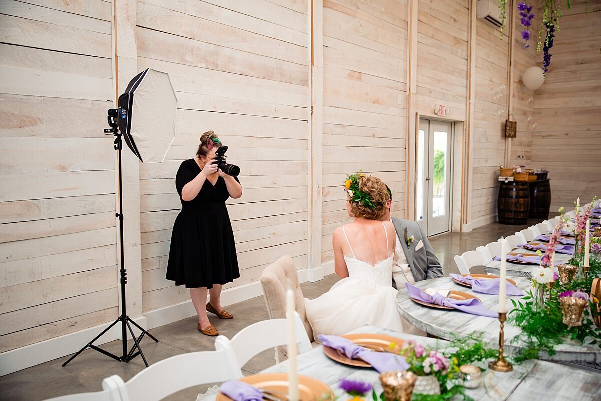 Behind the scenes photo of Mahlia with lighting equipment taking photo of couple inside White Dove Barn