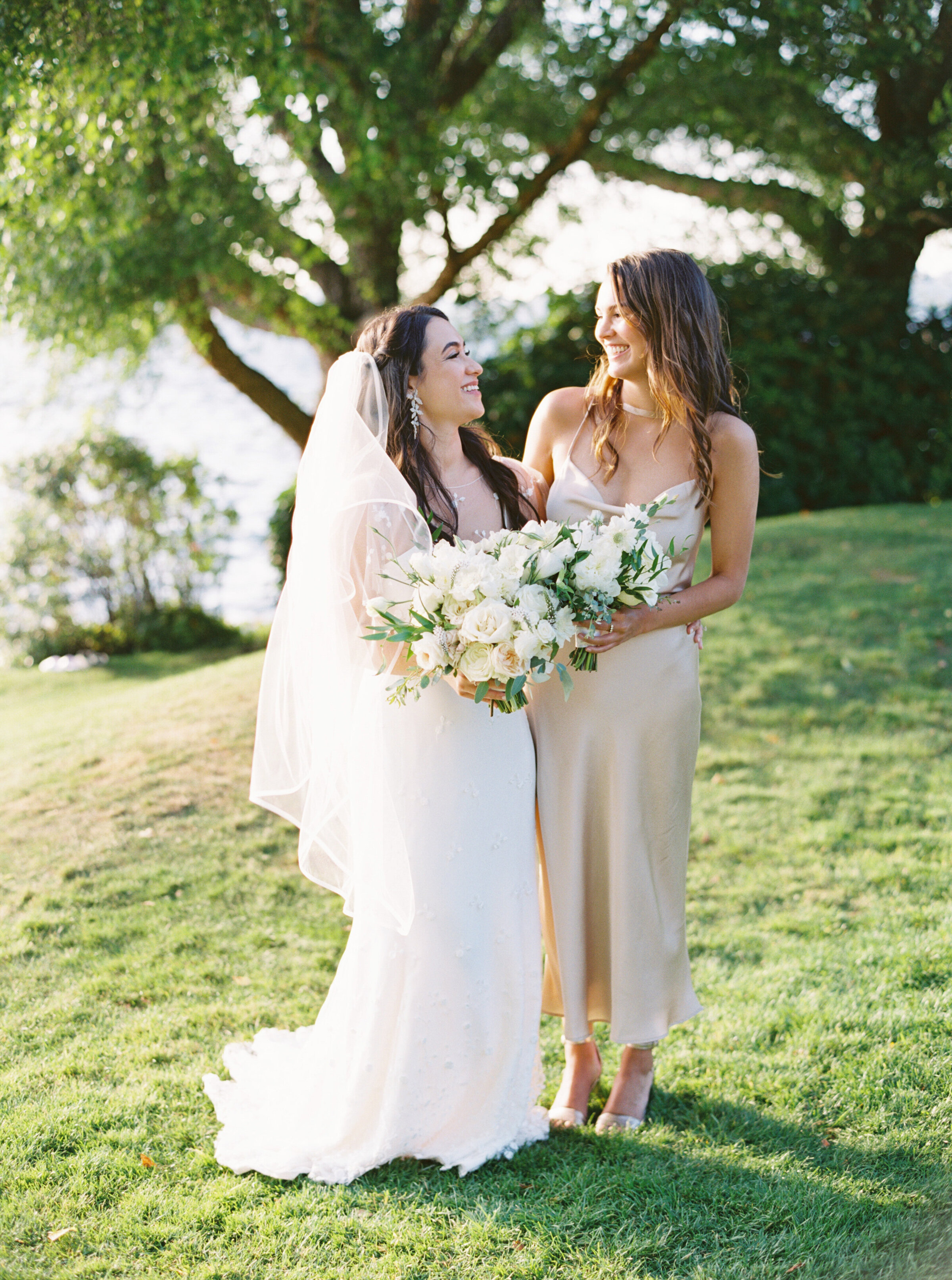 bride and bridesmaid laughing with each other holding white and green bouquet's