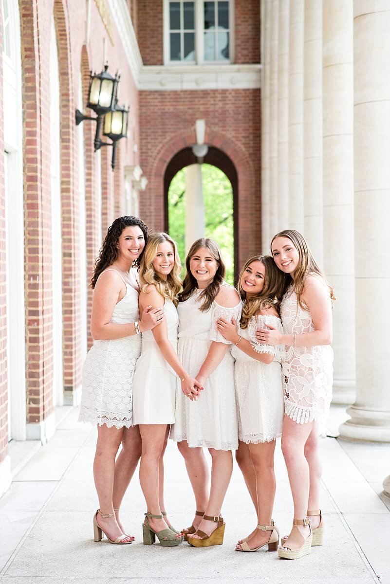 Group of 5 Vanderbilt seniors wearing white dresses and heels standing near large columns