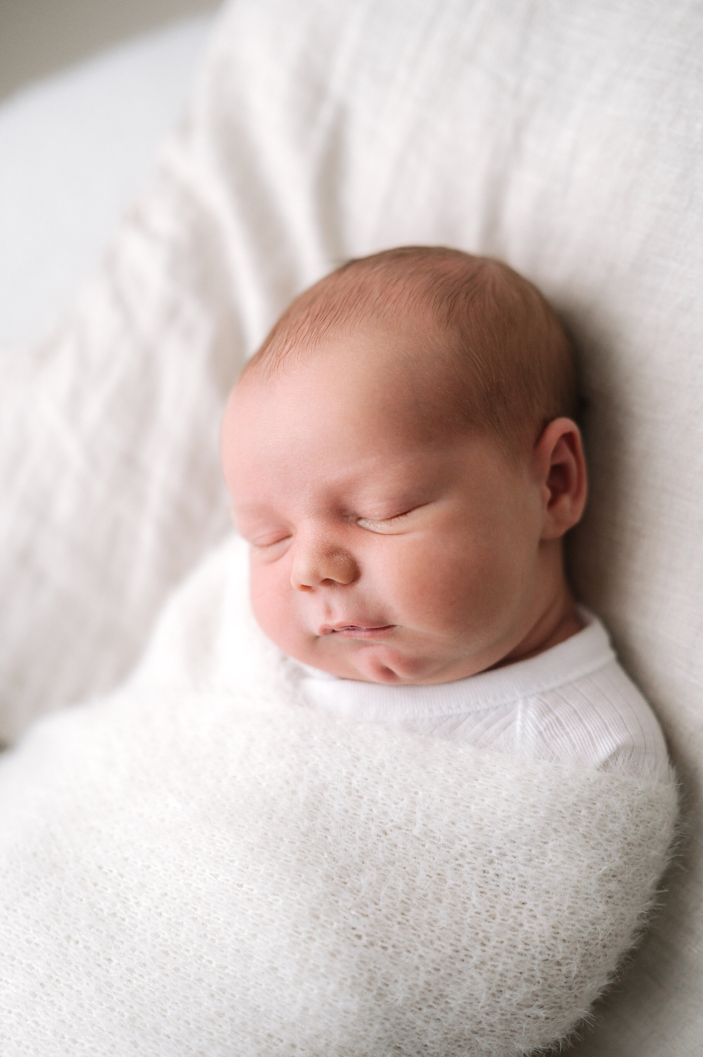 A newborn baby boy wrapped up in a white blanket during a photoshoot in Billingshurst