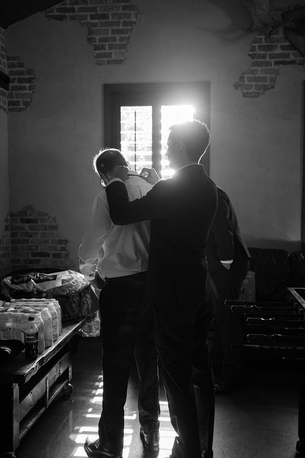 Groomsmen adjusting father of the brides collar in a moody black-and-white editorial image inside of The Chandelier of Gruene
