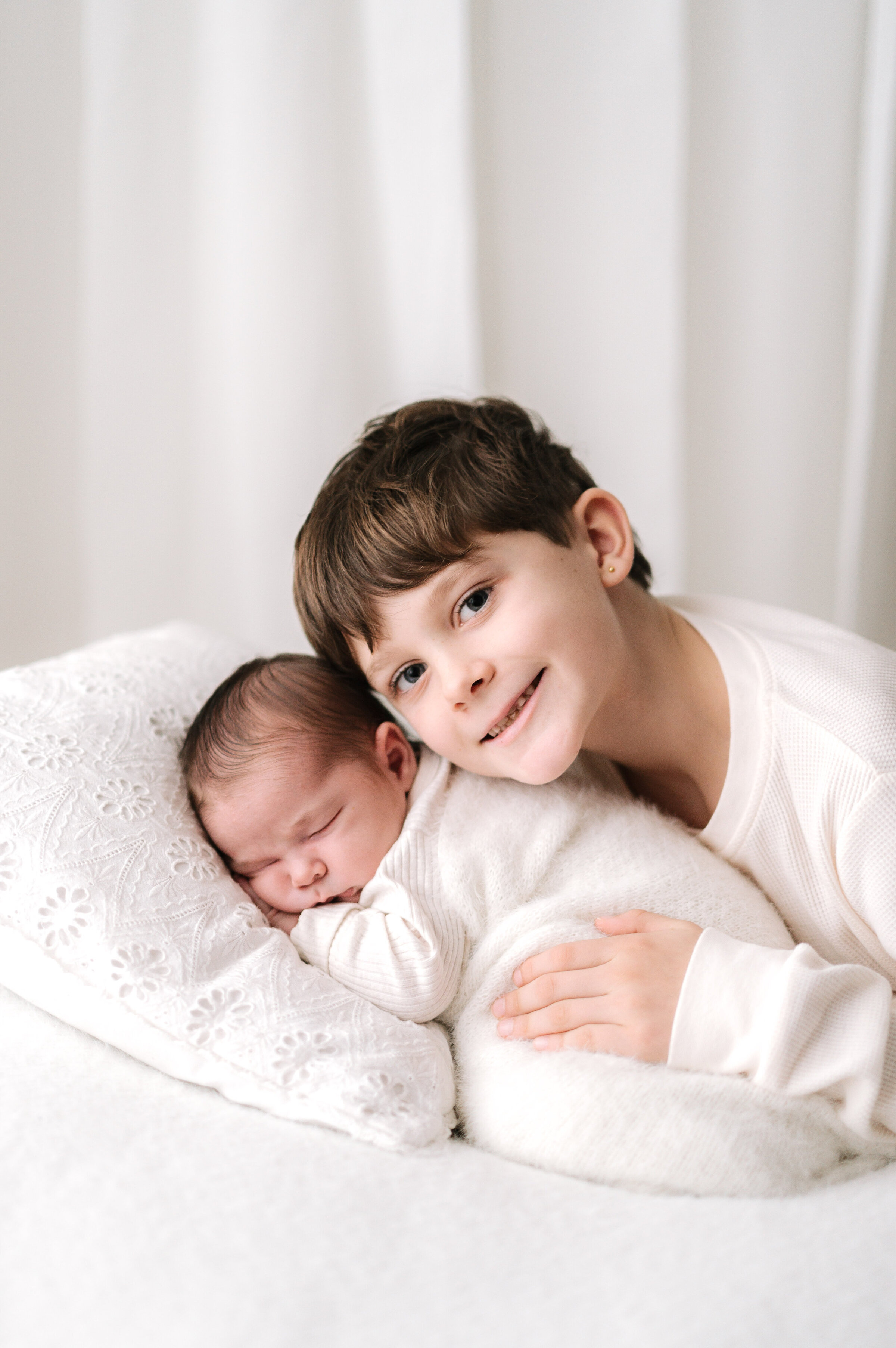 A older brother leaning over his younger sister at newborn photoshoot in Billingshurst