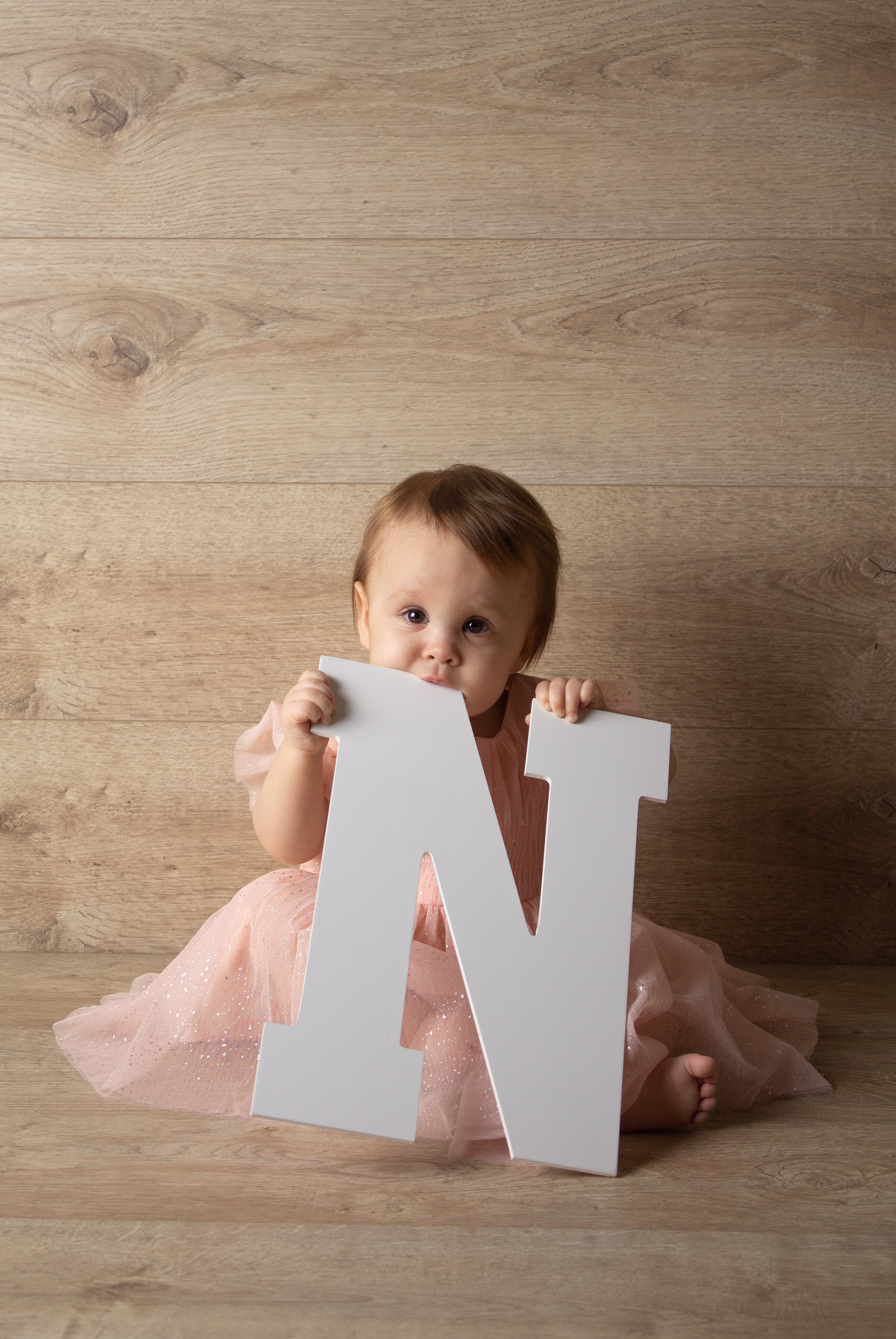 Cake smash session with Willow holding the letter N and biting down on the top of it.