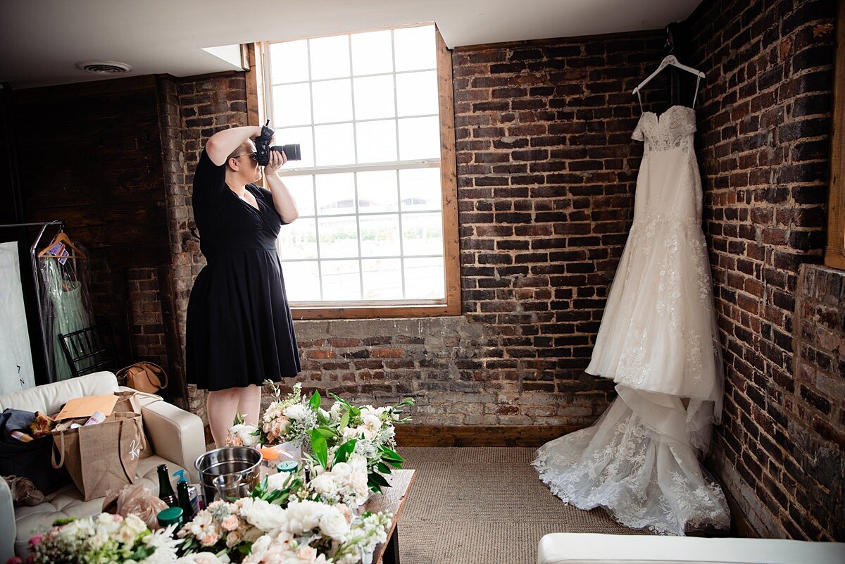 Mahlia taking photos of the wedding dress hanging on the brick wall