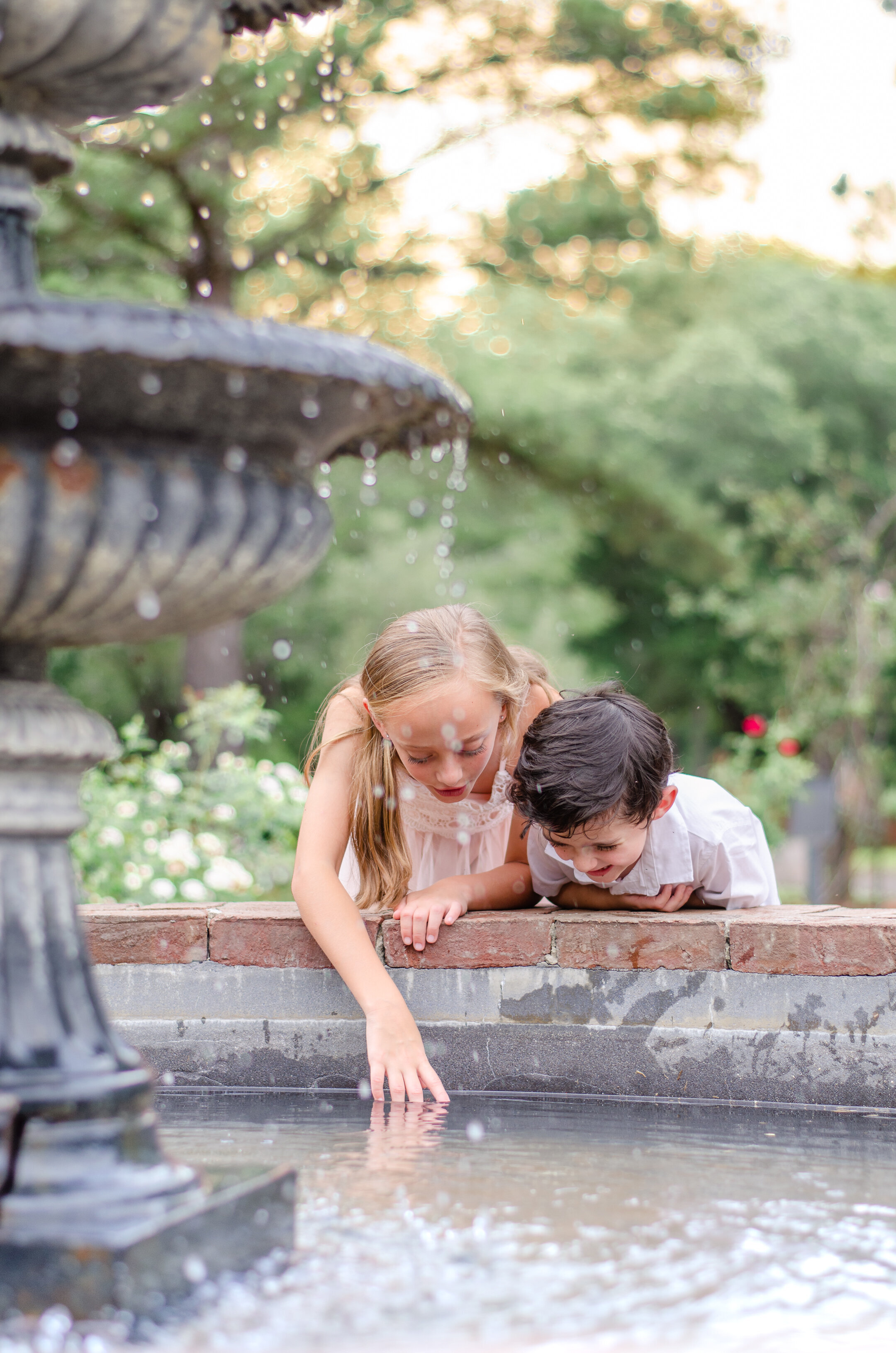 siblings look into a fairytale fountain in a rose garden in amsterdam