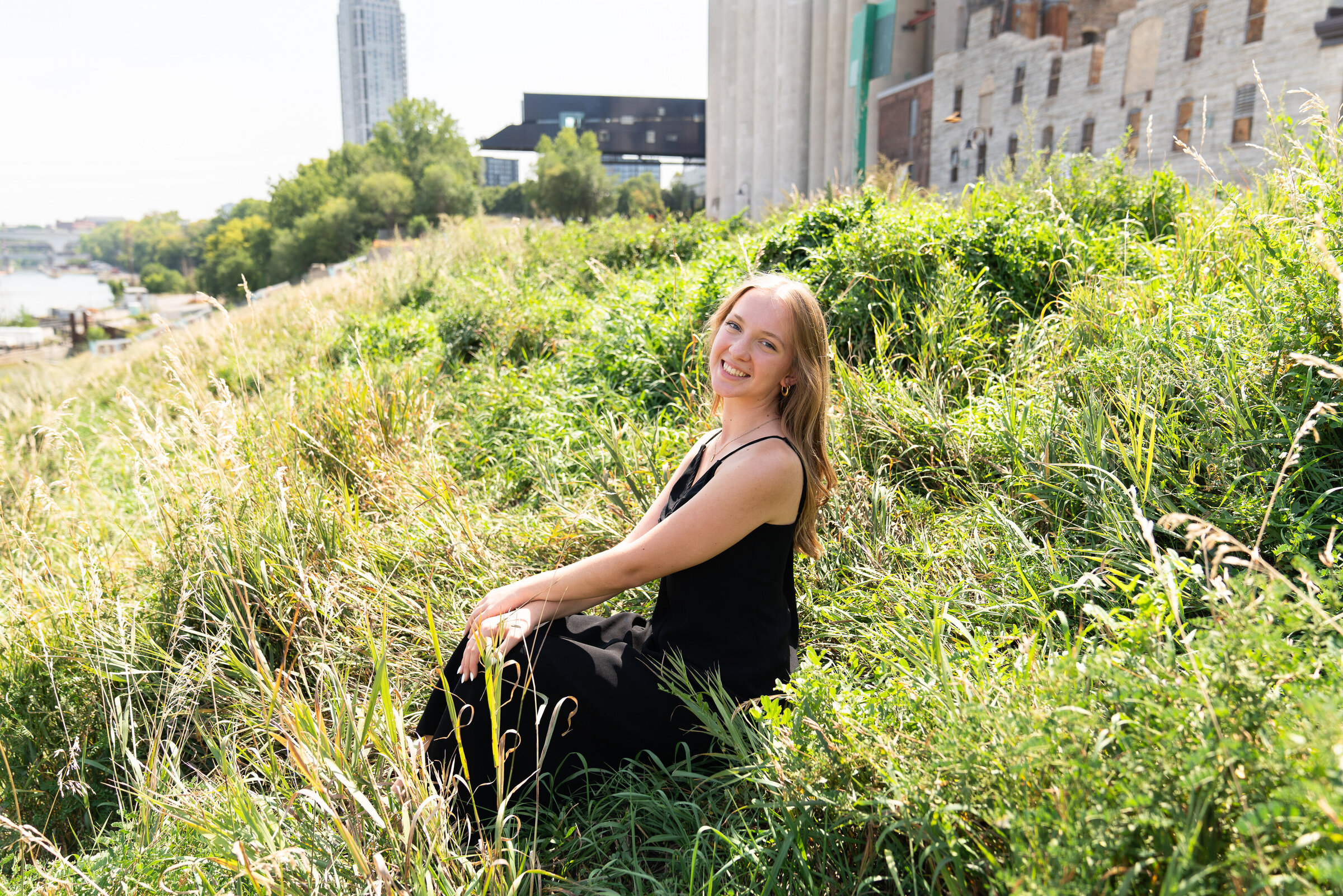 Girl sits in the the grass with the Mill City Ruins behind her